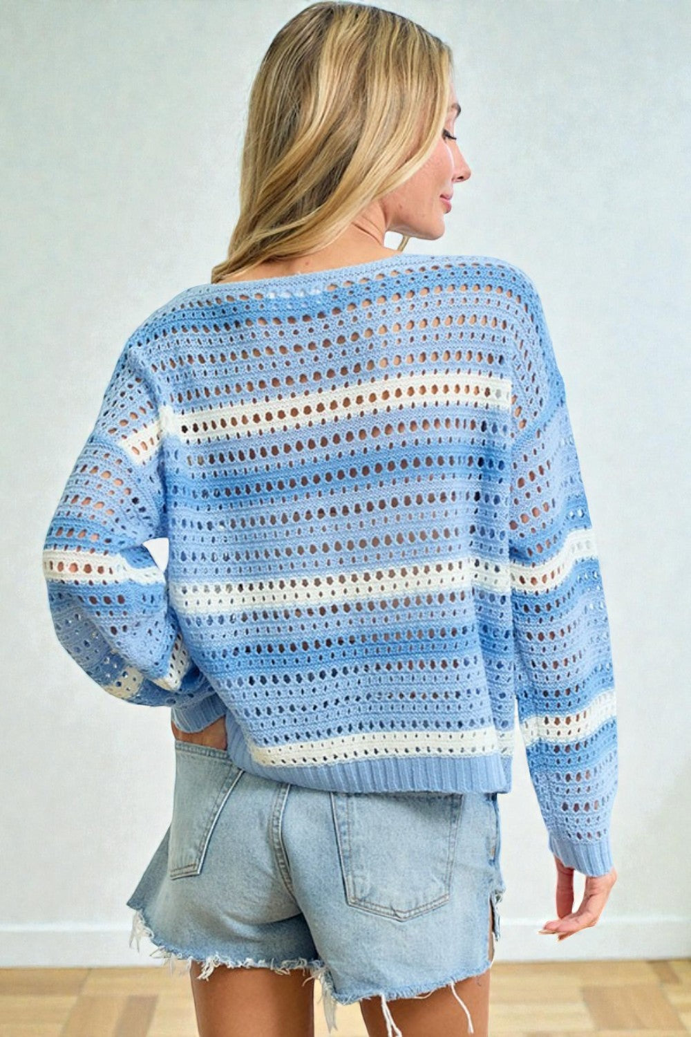 Woman wearing a blue crochet sweater with white stripes and denim shorts against a light background