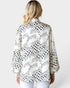 Woman wearing a patterned blouse with black and white designs on a plain background