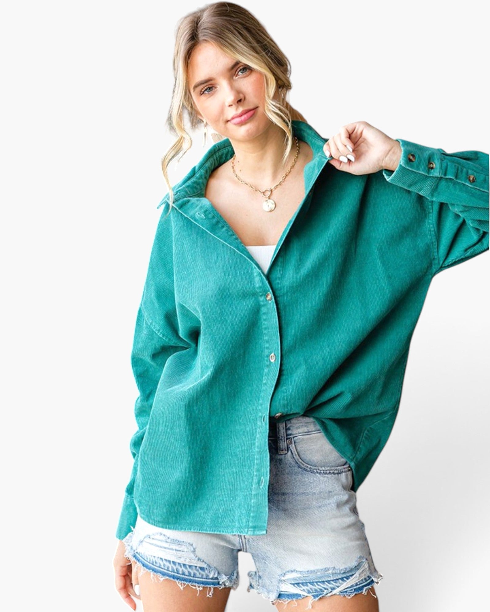 A woman wearing an oversized teal-green button-up shirt with denim shorts, posing against a clean white background.