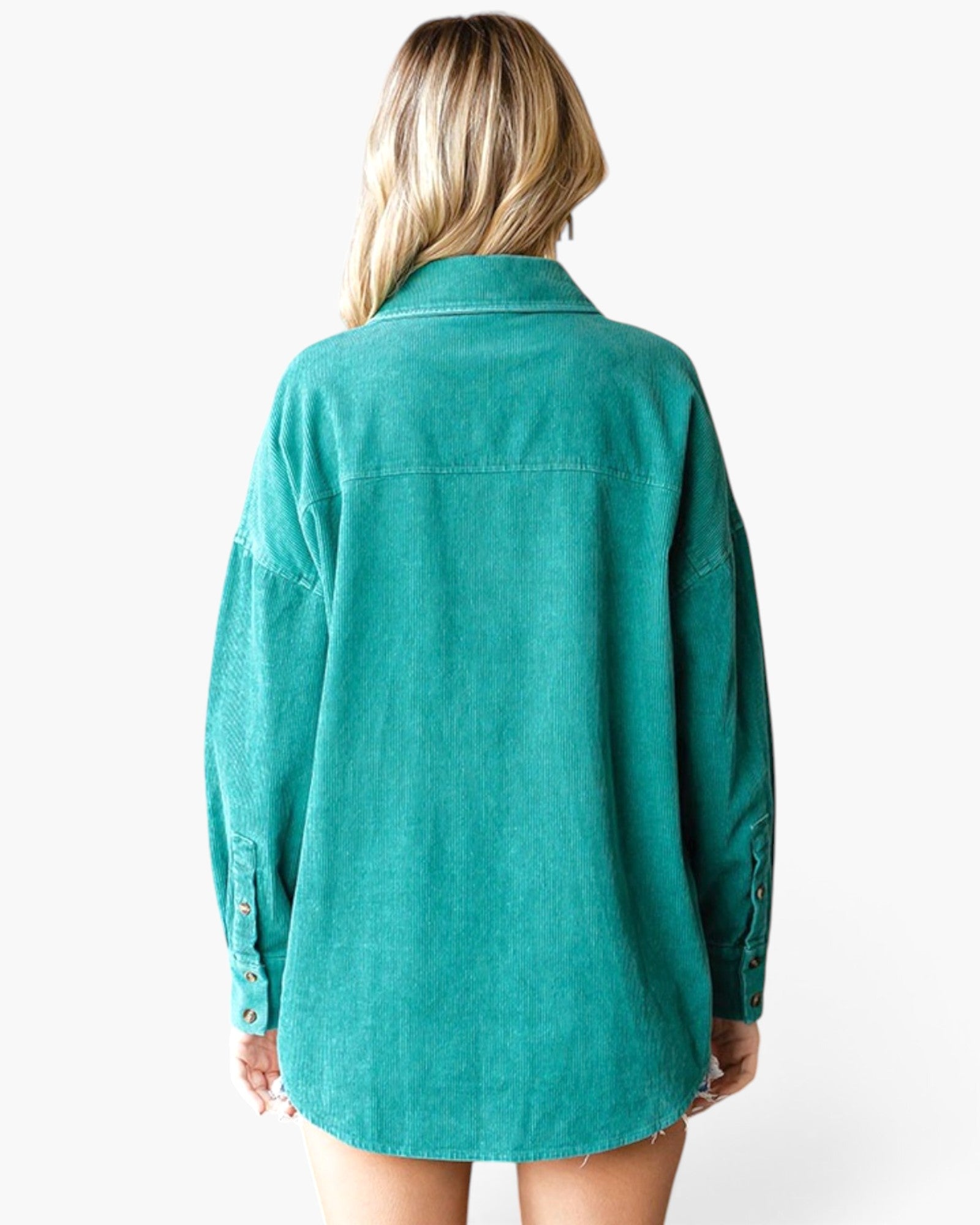 A woman viewed from the back wearing an oversized teal-green button-up shirt with long sleeves and a raw hem, set against a plain white studio background.