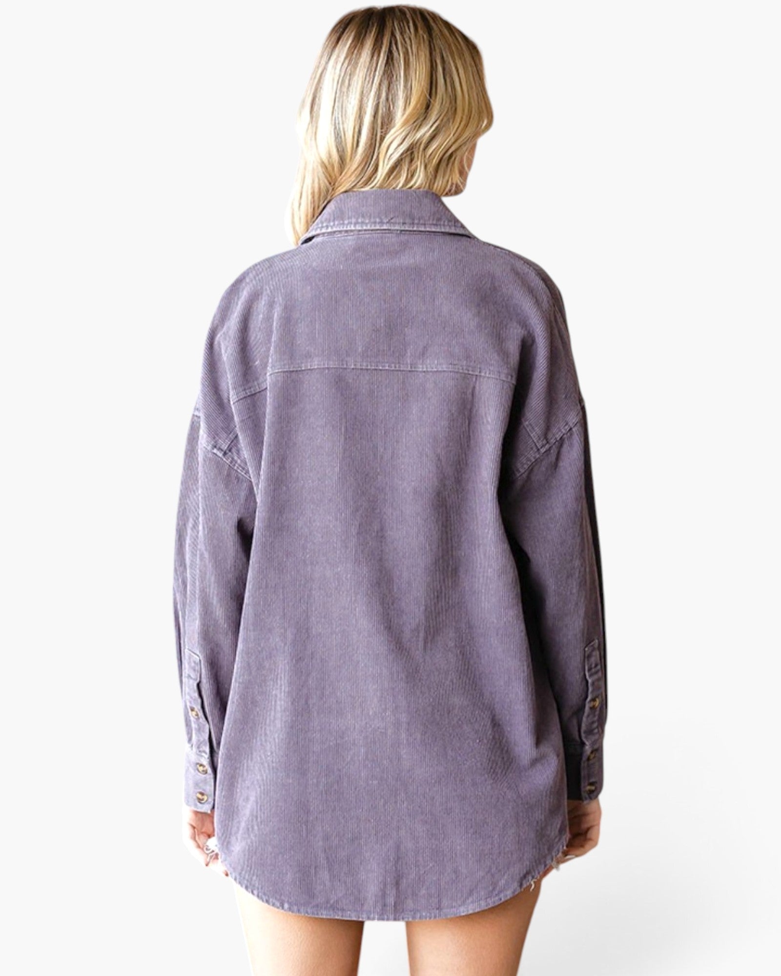 A woman viewed from the back wearing an oversized, long-sleeve button-up shirt in a muted dusty lavender-purple color, set against a plain white studio background.