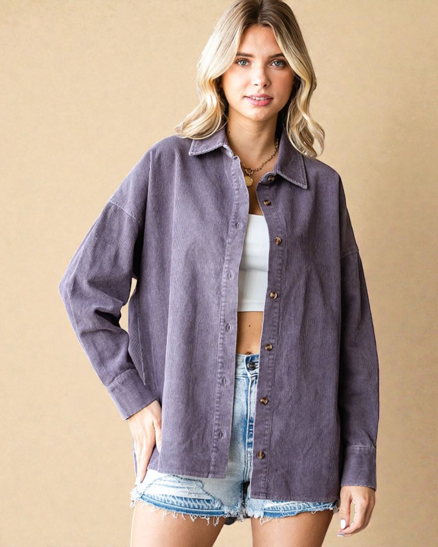 Woman wearing a purple denim jacket over a white top and denim shorts on a beige background