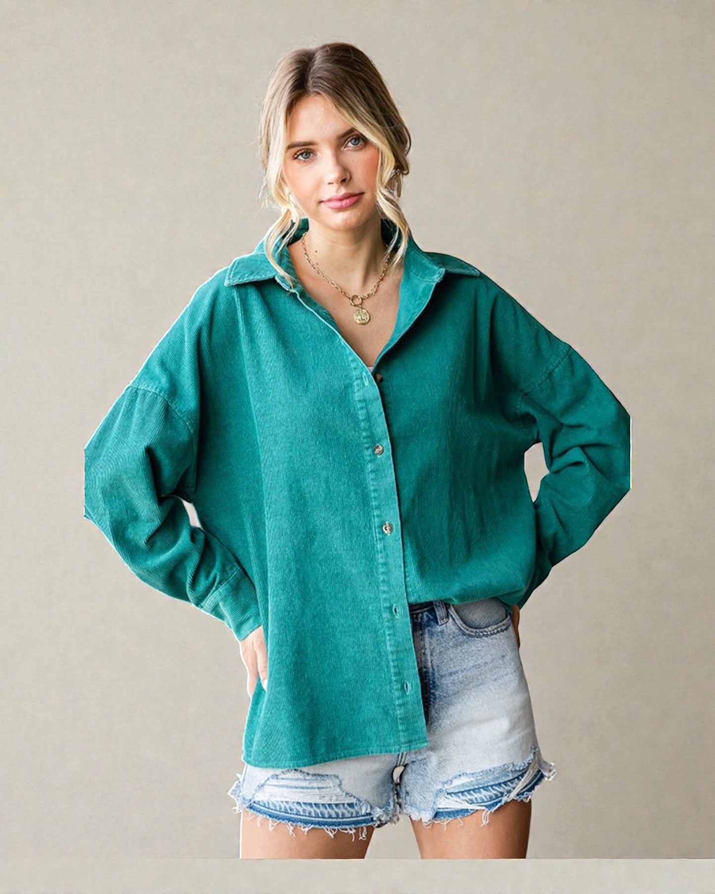 Woman wearing a teal shirt and denim shorts against a beige background