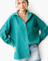 A woman wearing an oversized teal-green button-up shirt with light-wash denim jeans, photographed against a plain white background.