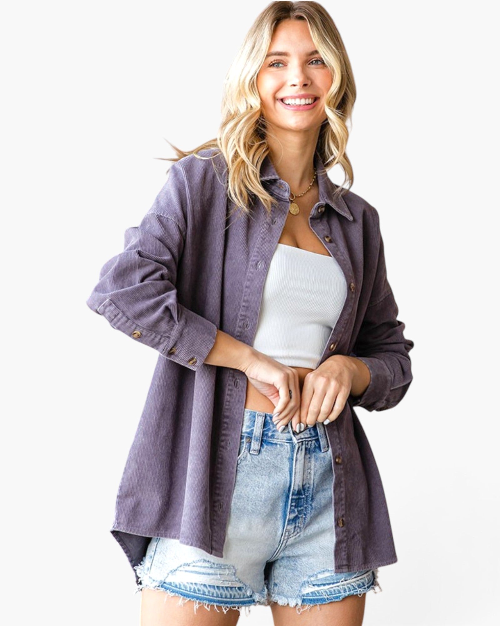 A woman modeling a loose-fitting, long-sleeve button-up shirt in a muted dusty purple or mauve shade, worn open over a white tank top and light-wash denim shorts, against a plain white studio background.