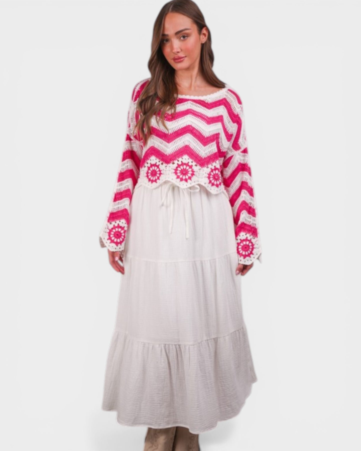 Woman wearing a pink and white patterned sweater with a long light gray skirt on a white background