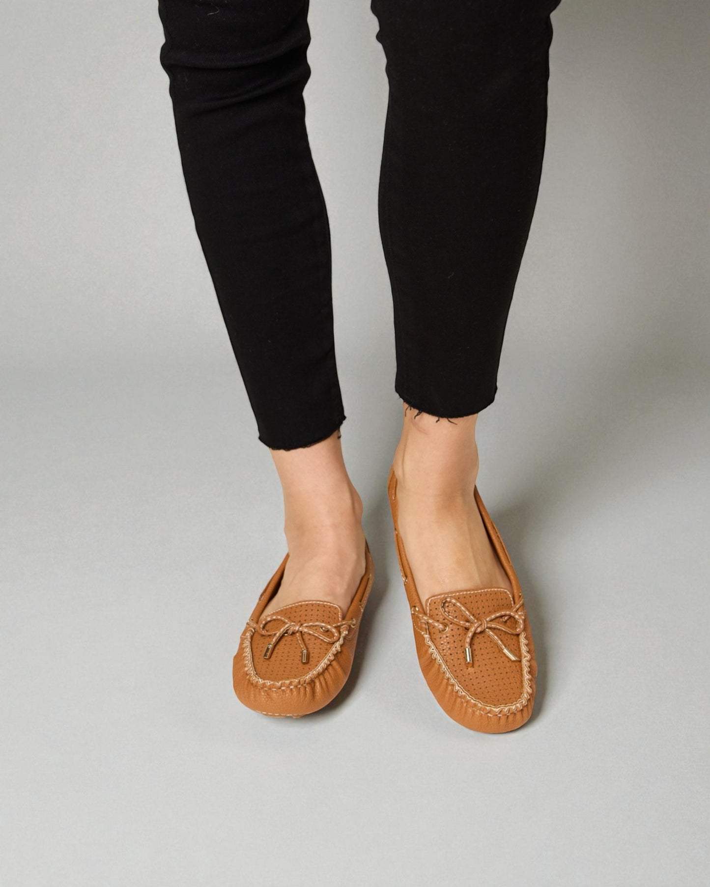 Brown loafers worn with black pants on a gray background