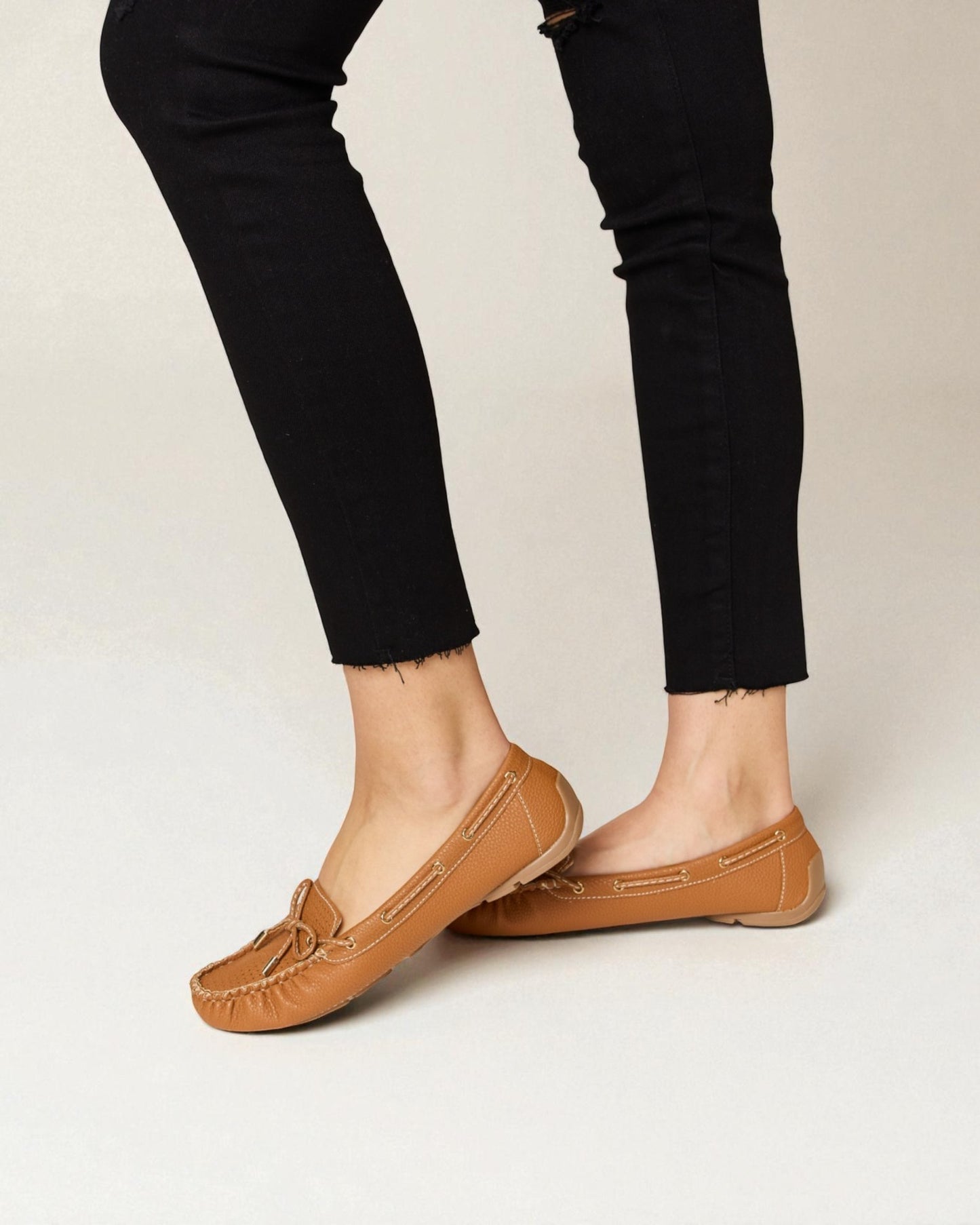 Brown loafers worn with black pants on a light background