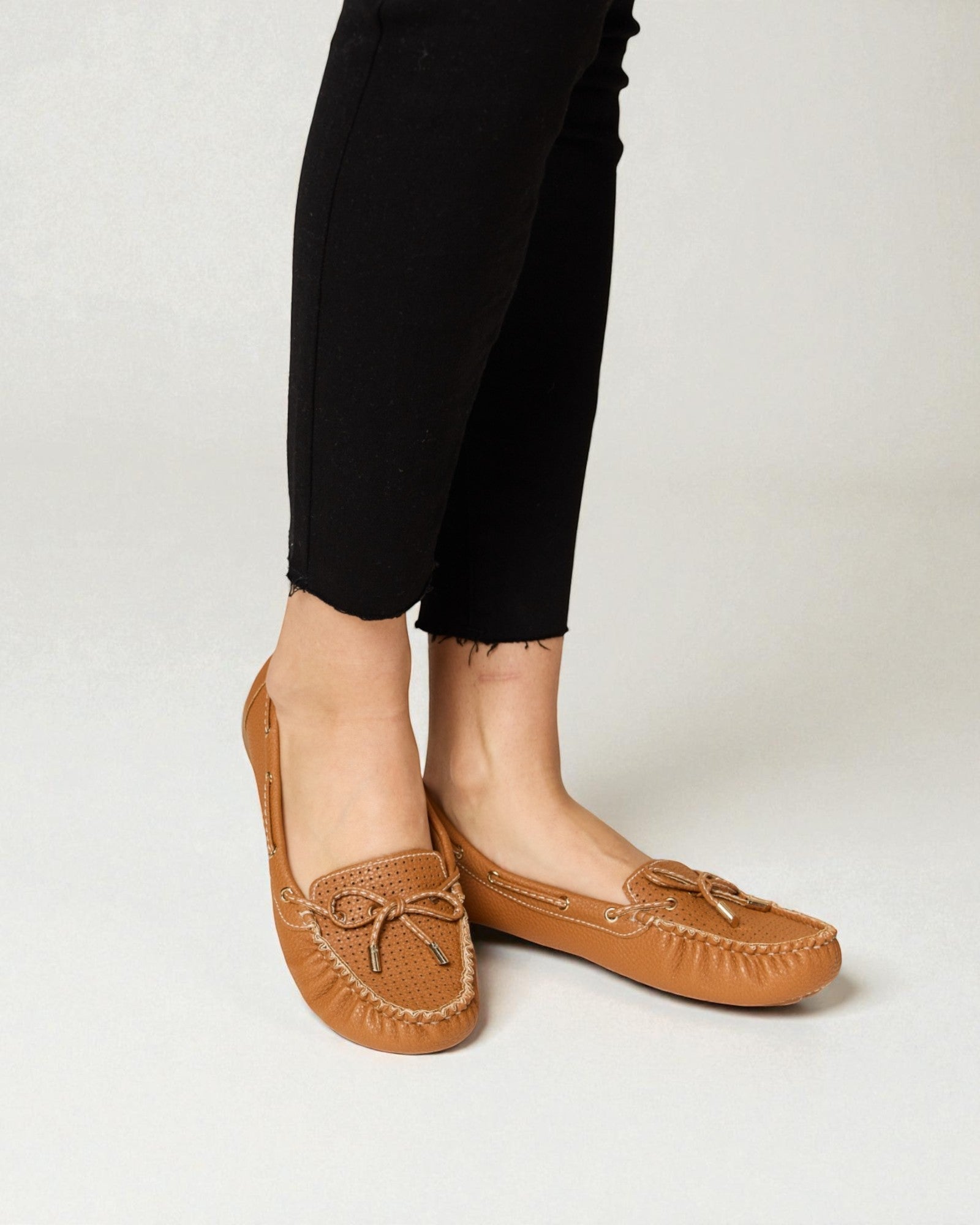 Brown moccasin shoes worn with black pants on a light background