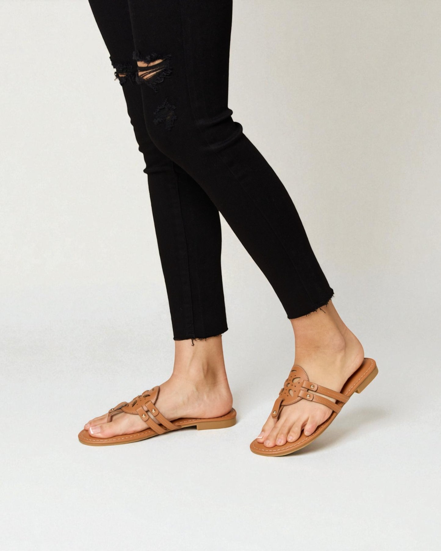Person wearing black distressed jeans and tan sandals on a white background