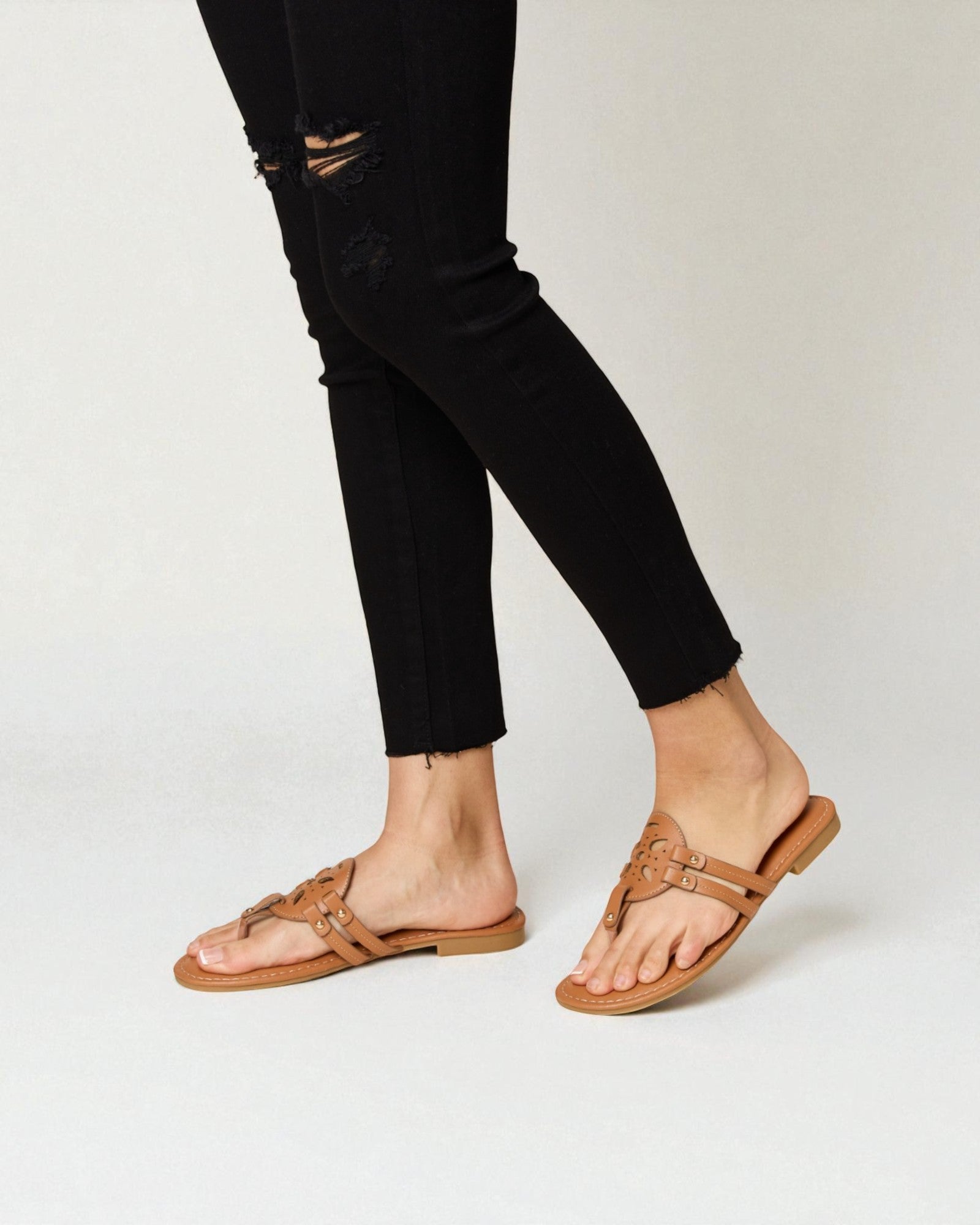 Person wearing black distressed jeans and tan sandals on a white background