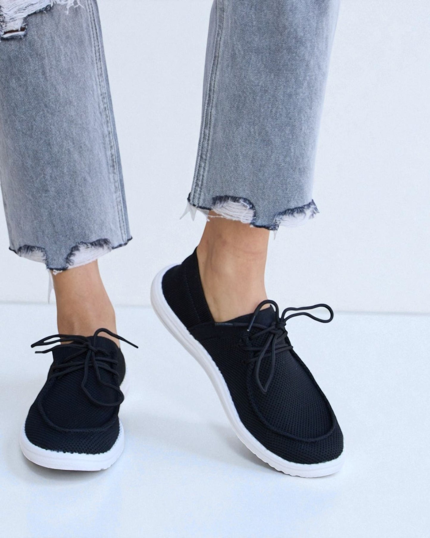 Black sneakers worn with light blue jeans on a white background