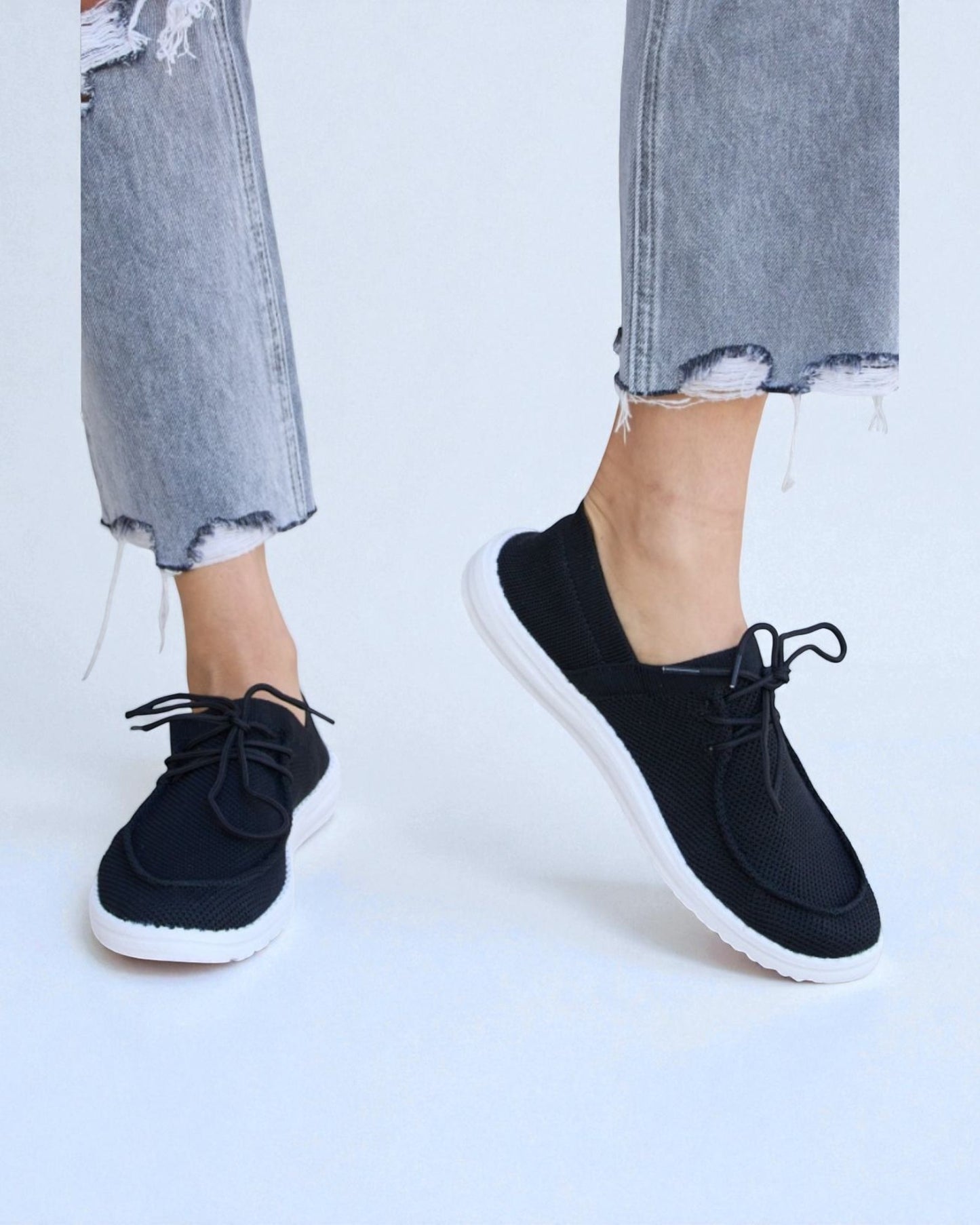 Black sneakers worn with light blue jeans on a white background