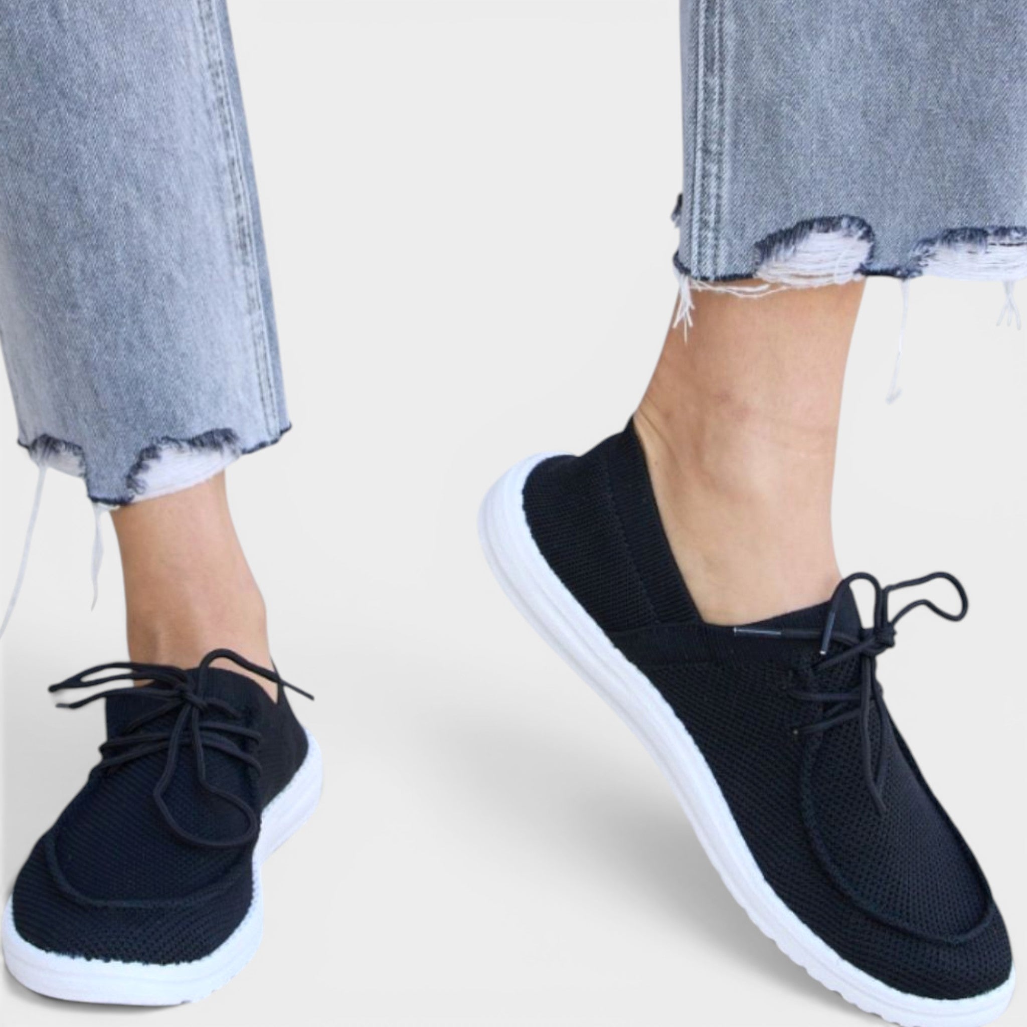 Navy blue sneakers with white soles worn with light blue jeans on a white background
