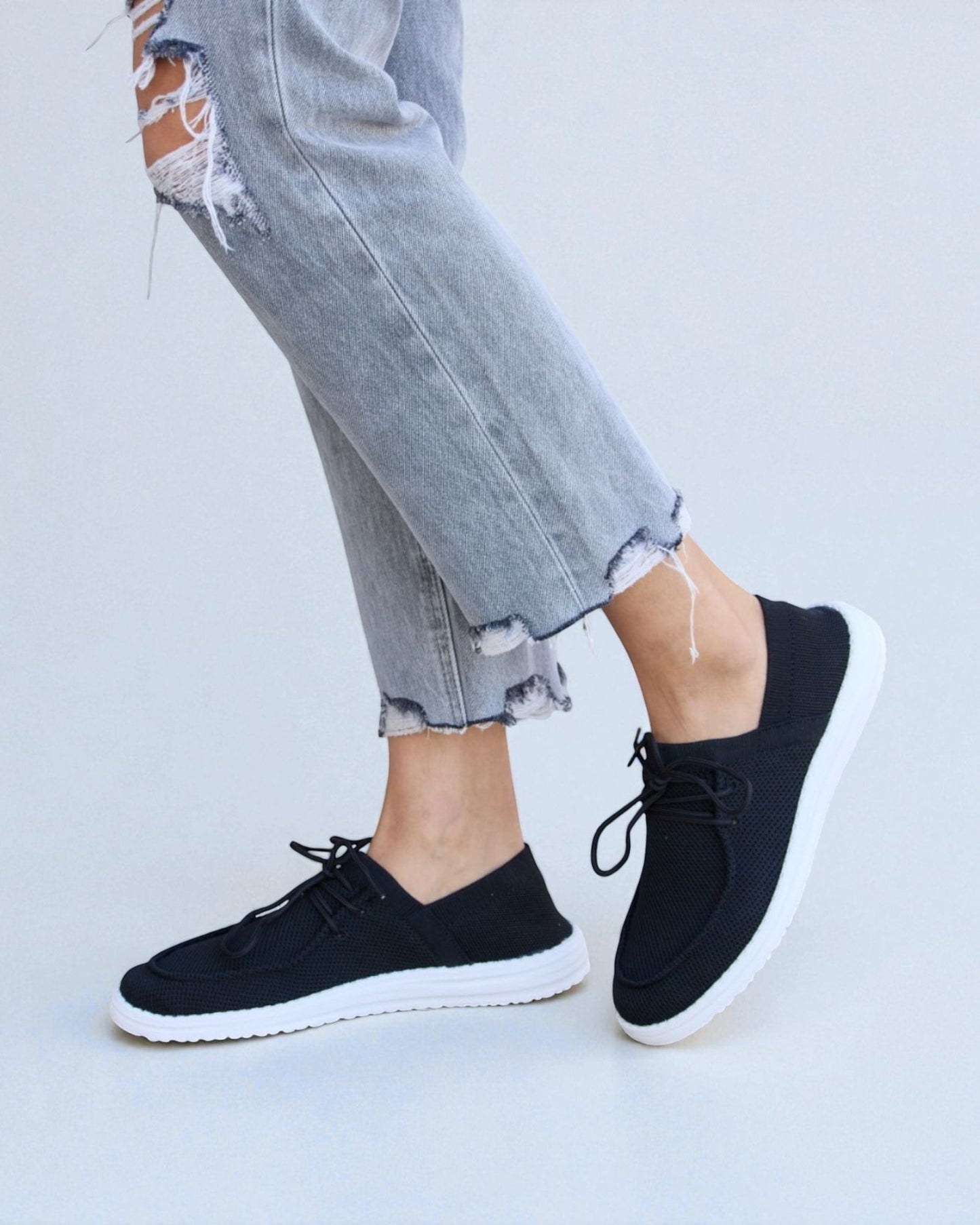 Black sneakers worn with ripped jeans on a light gray background