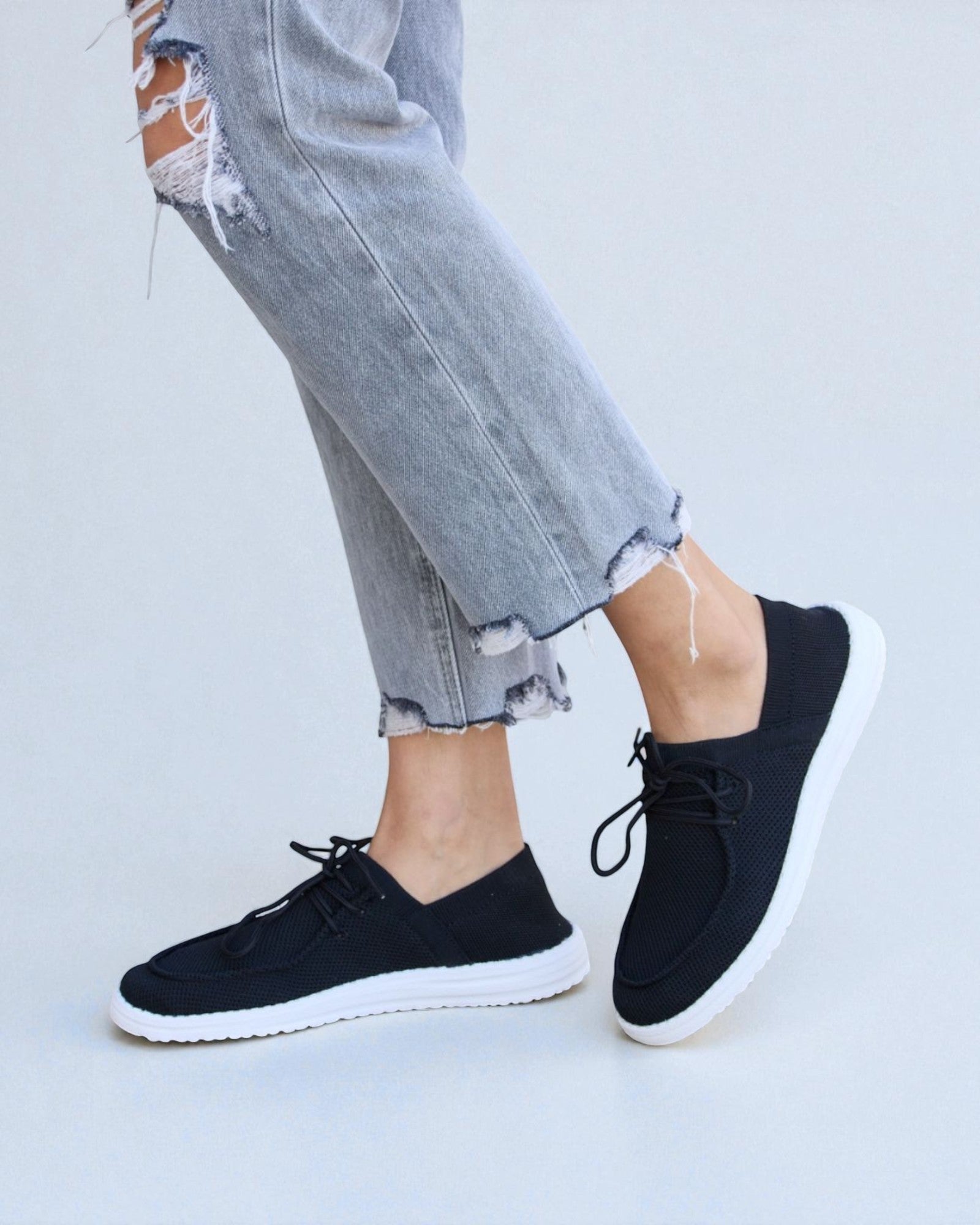 Black sneakers worn with ripped jeans on a light gray background