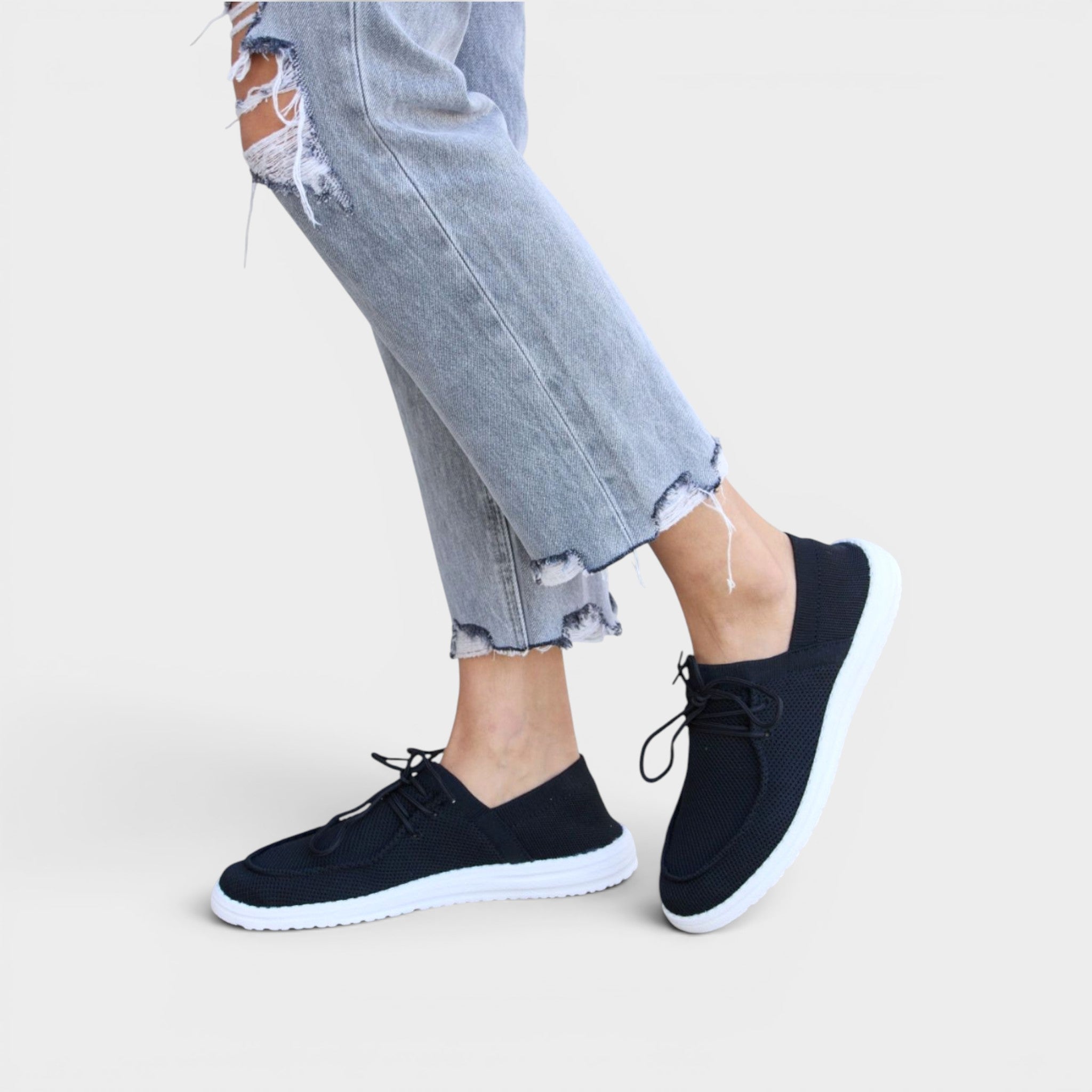 Person wearing black sneakers with white soles on a light background