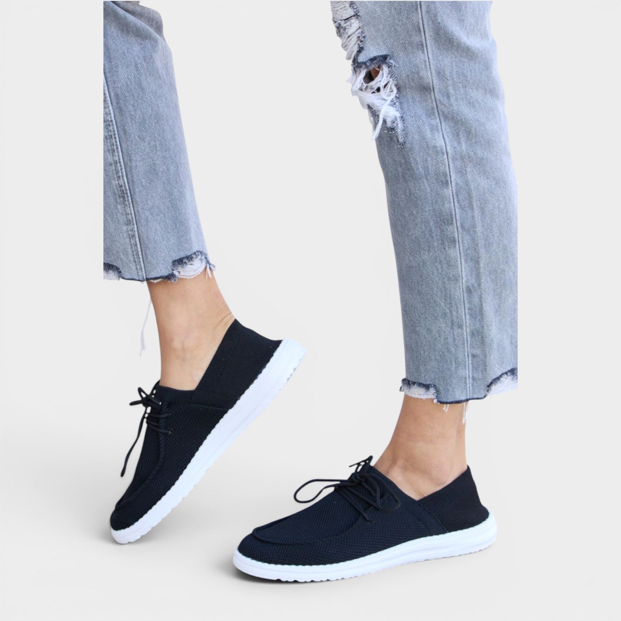 Black sneakers worn with ripped jeans on a light background