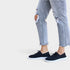 Person wearing ripped jeans and navy sneakers on a plain background