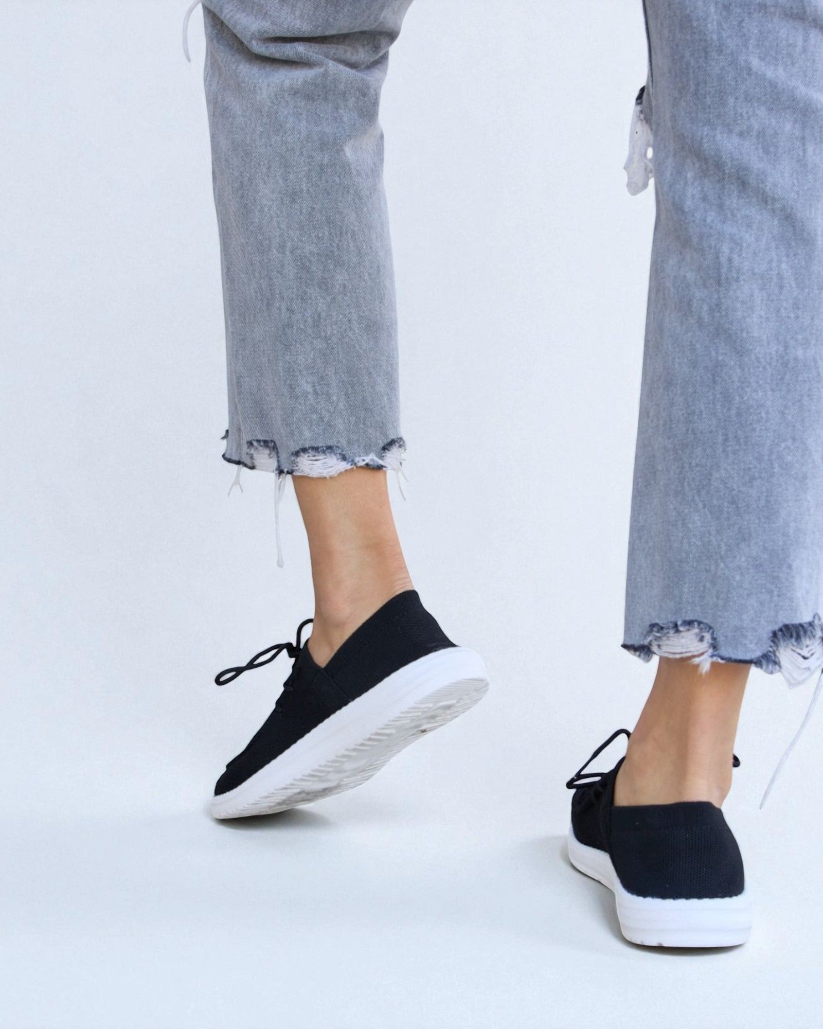 Black slip-on shoes worn with light blue jeans on a white background