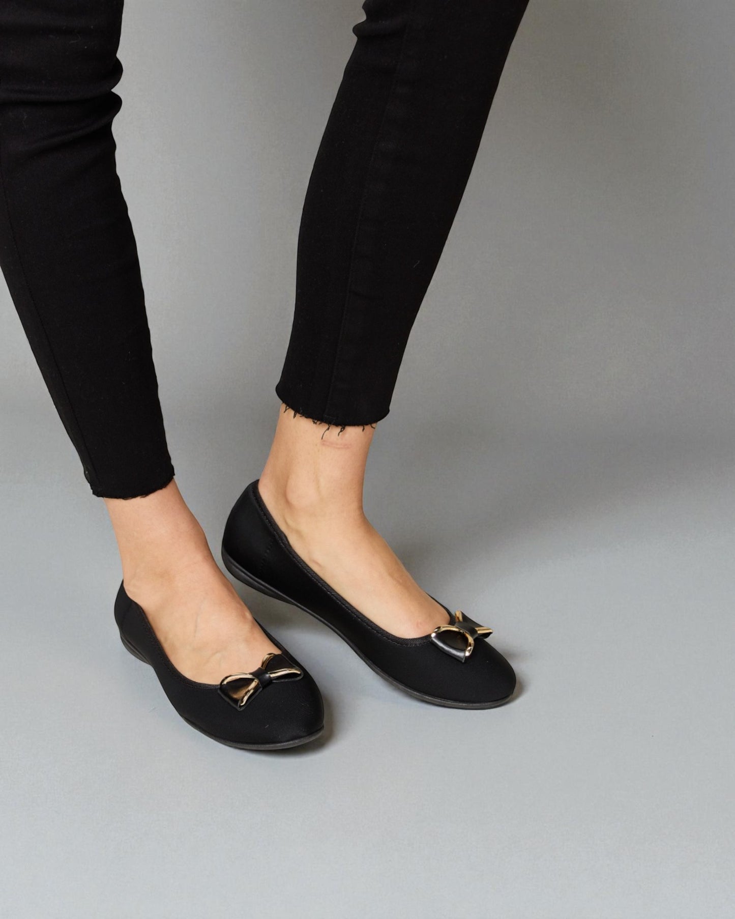 Black flats with gold buckles worn with black pants on a gray background