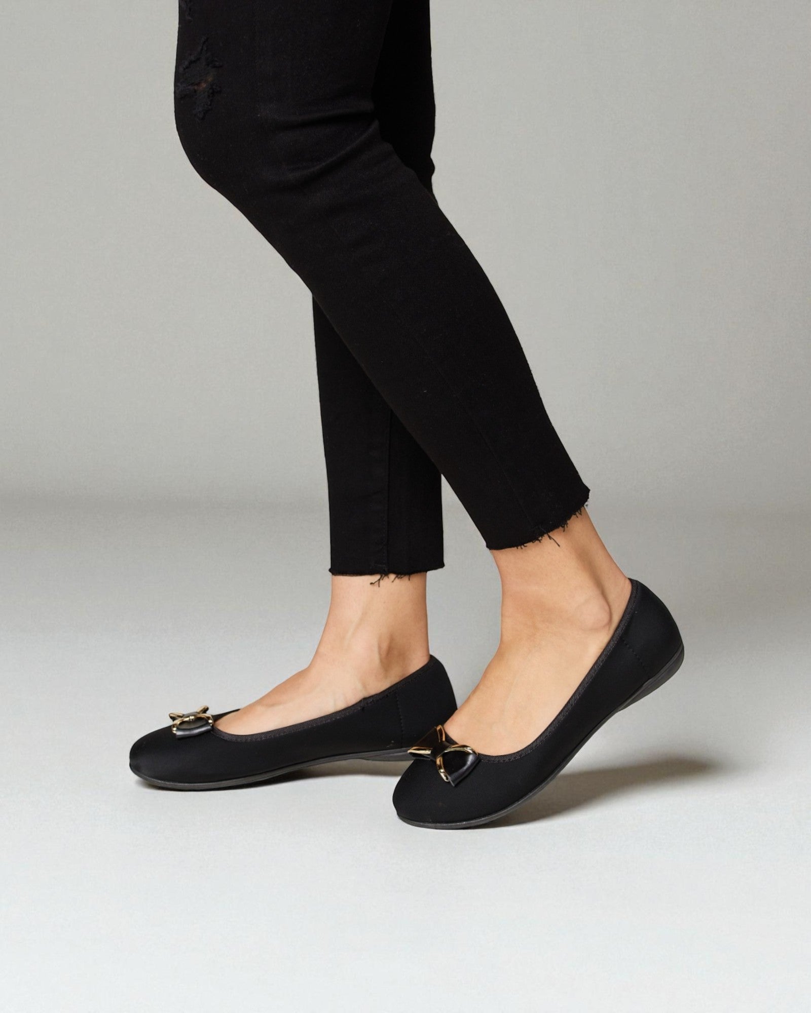 Black flats worn with black pants on a neutral background
