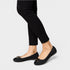 Black flats worn with black pants on a light gray background