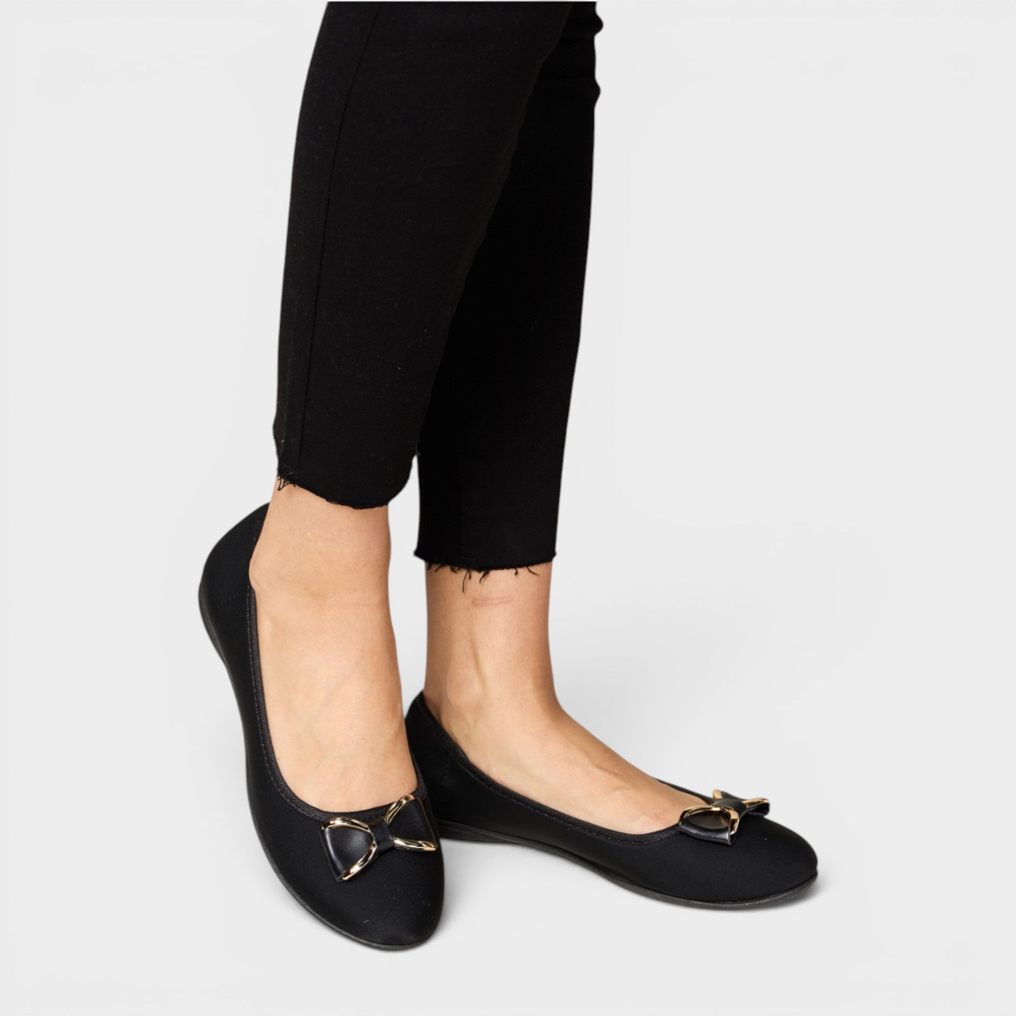 Black flats with bow details worn with black pants on a light gray background