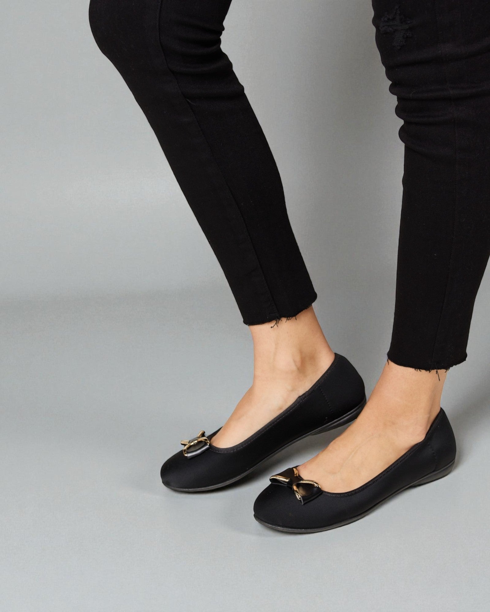 Black flat shoes worn with black pants on a gray background