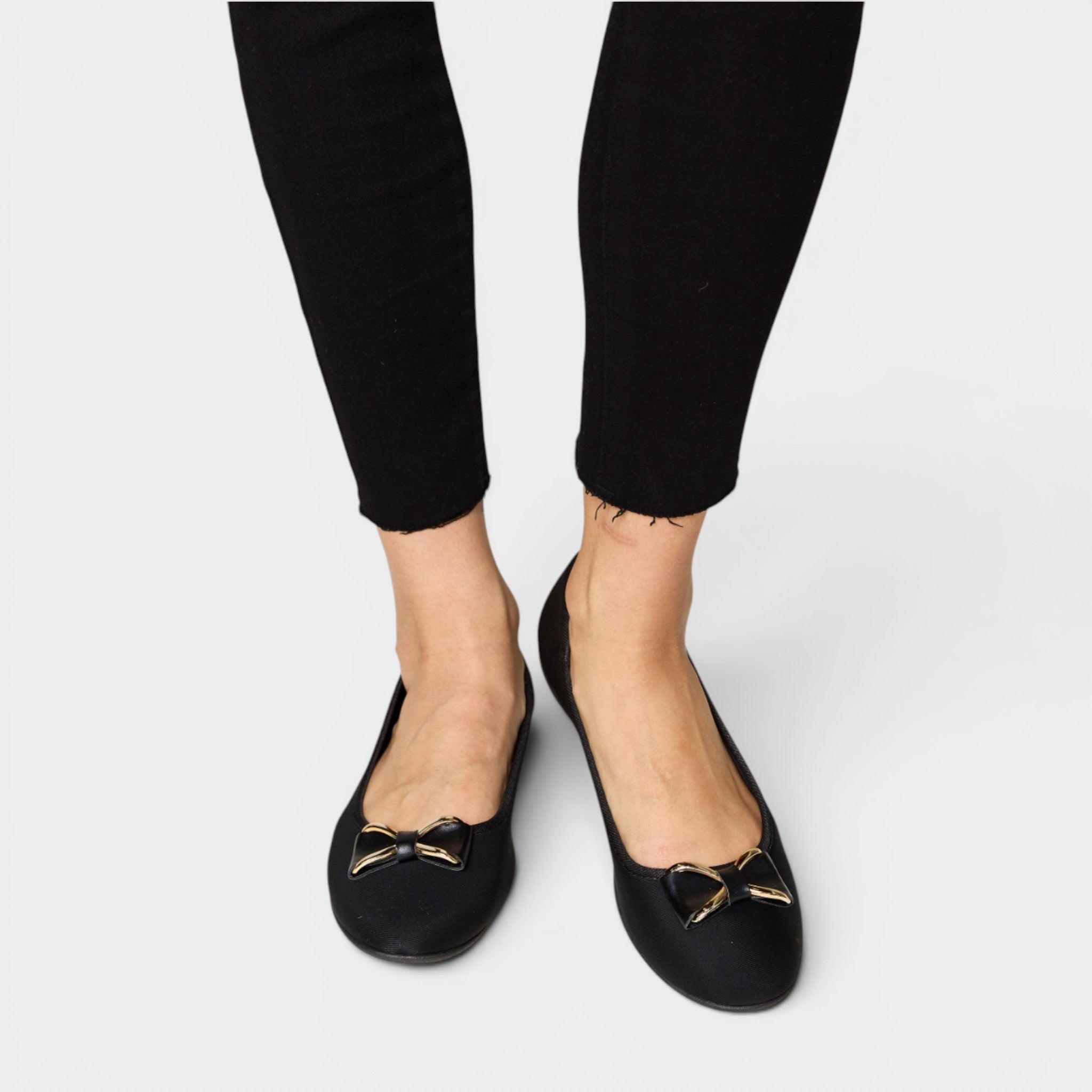 Black flats with gold bows worn with black pants on a white background