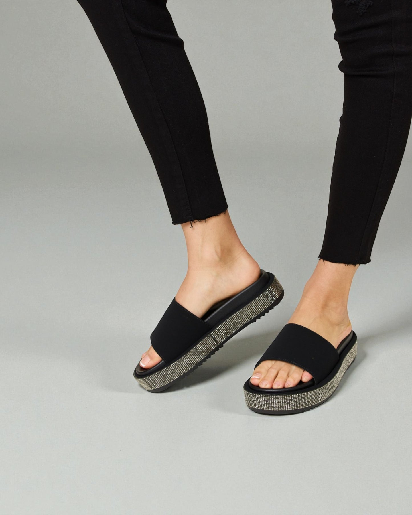 Black sandals with textured sole worn by a person on a gray background