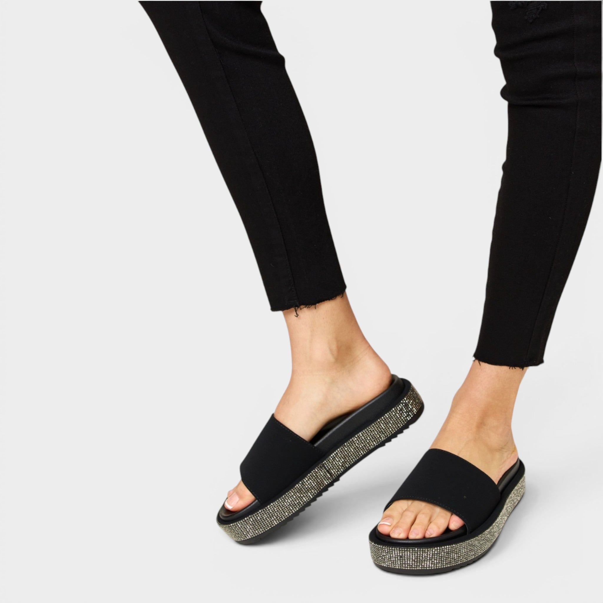 Black sandals with glittery sole worn with black pants on a light gray background
