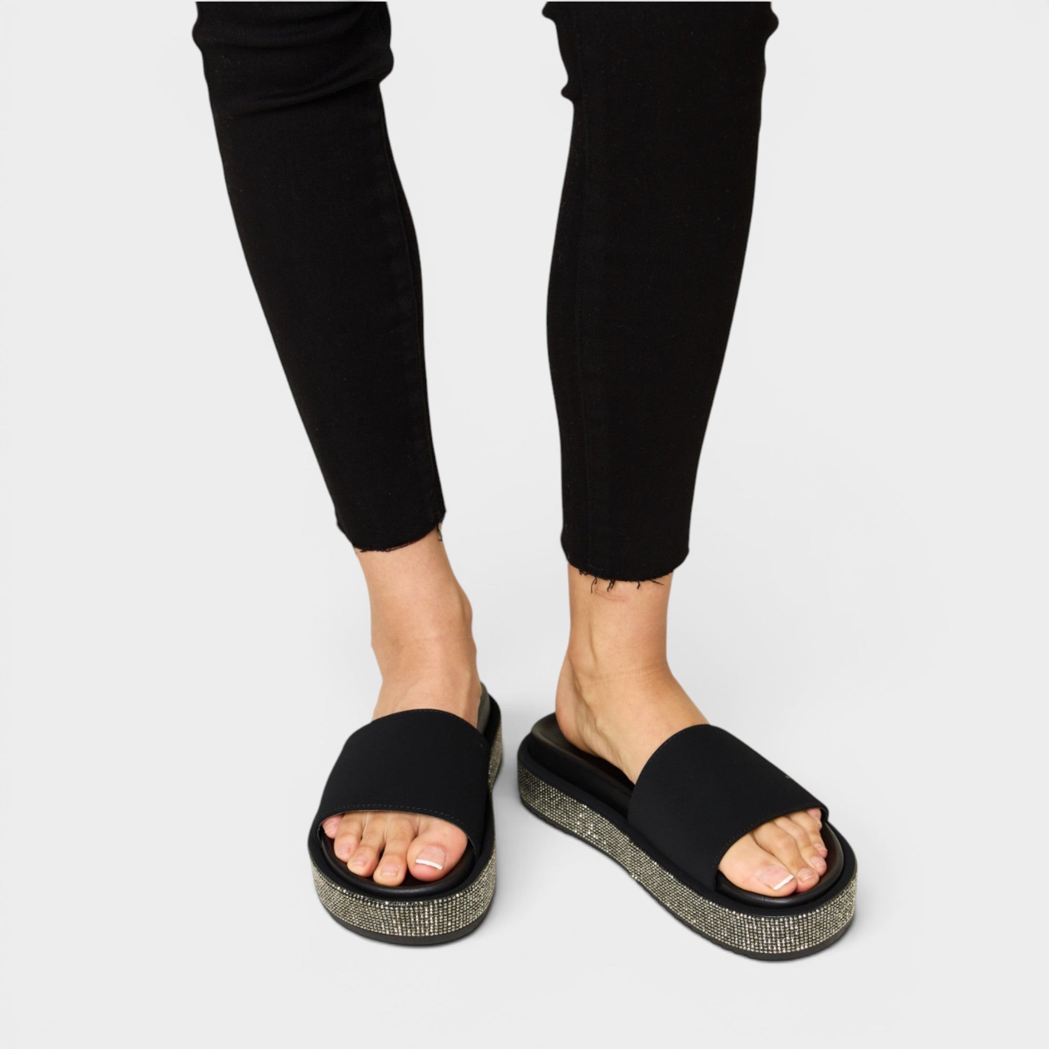 Black sandals worn with black pants on a white background
