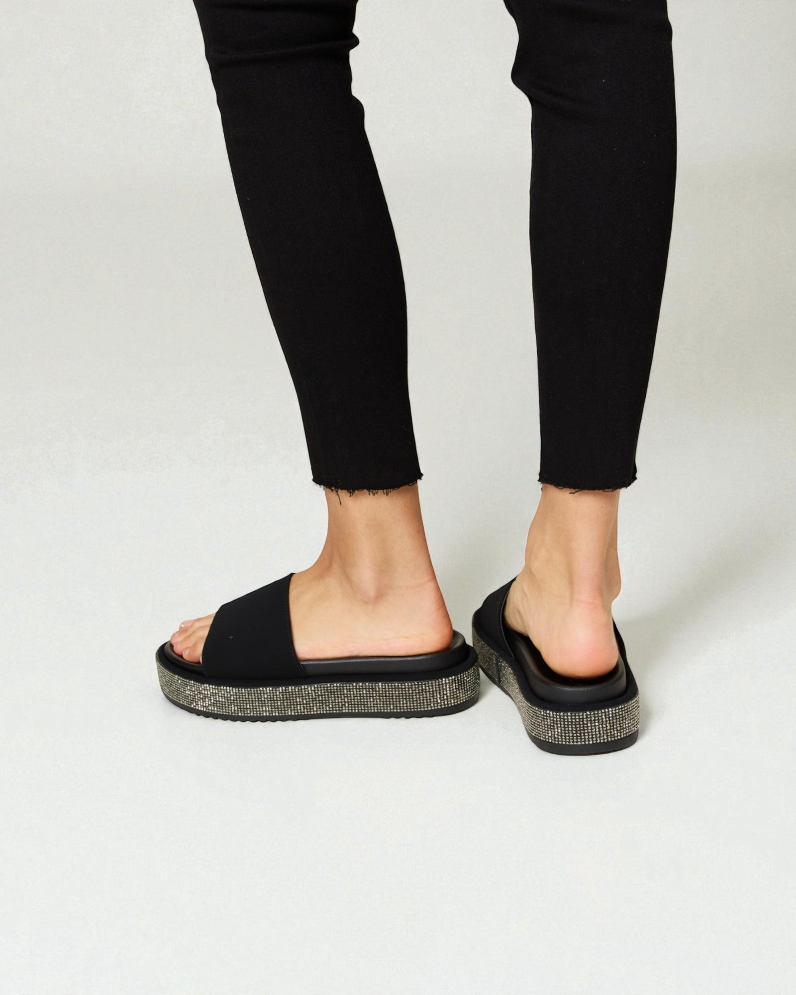 Black sandals worn with black pants on a white background