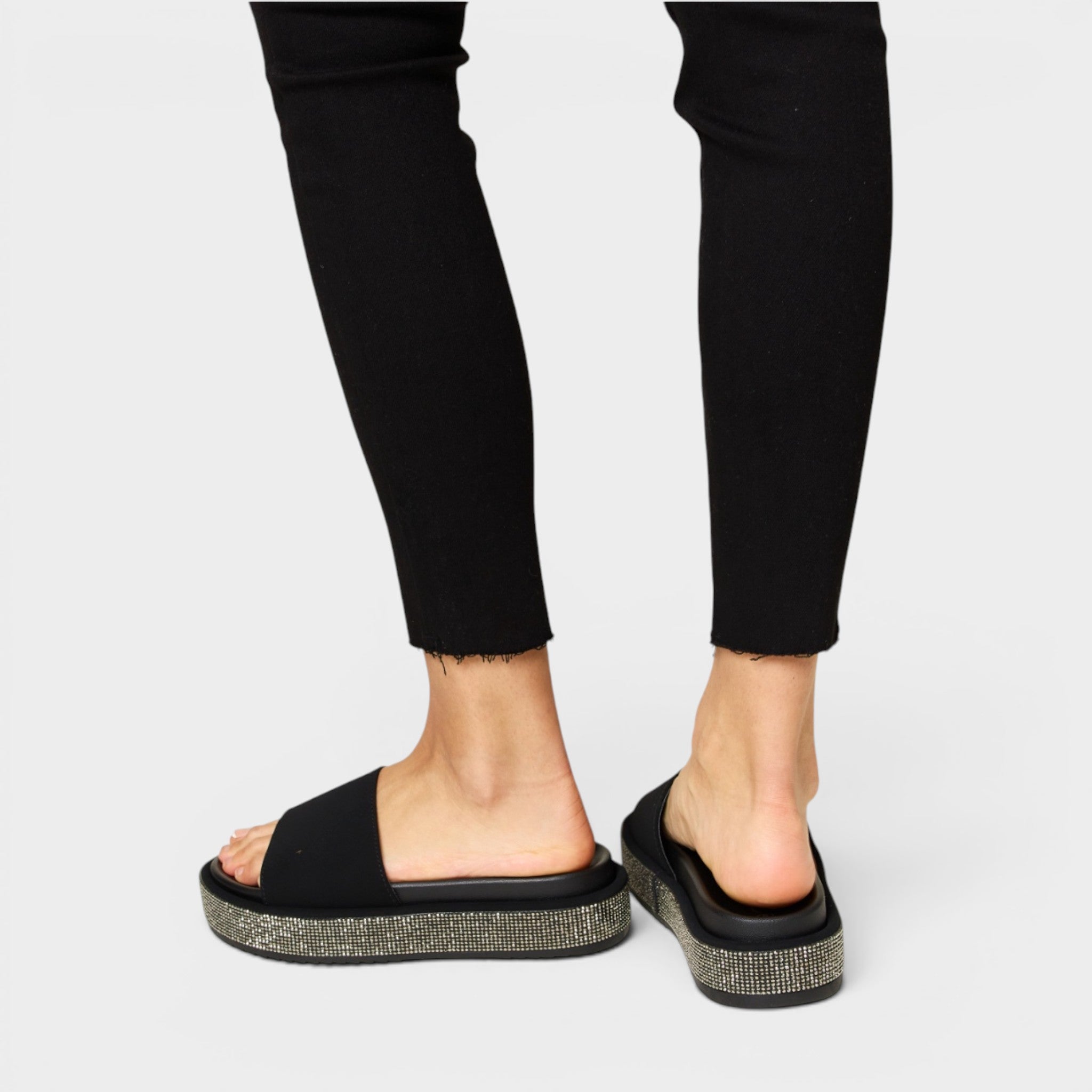 Black sandals with glittery sole worn with black pants on a light gray background