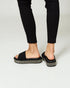 Black sandals worn with black pants on a white background