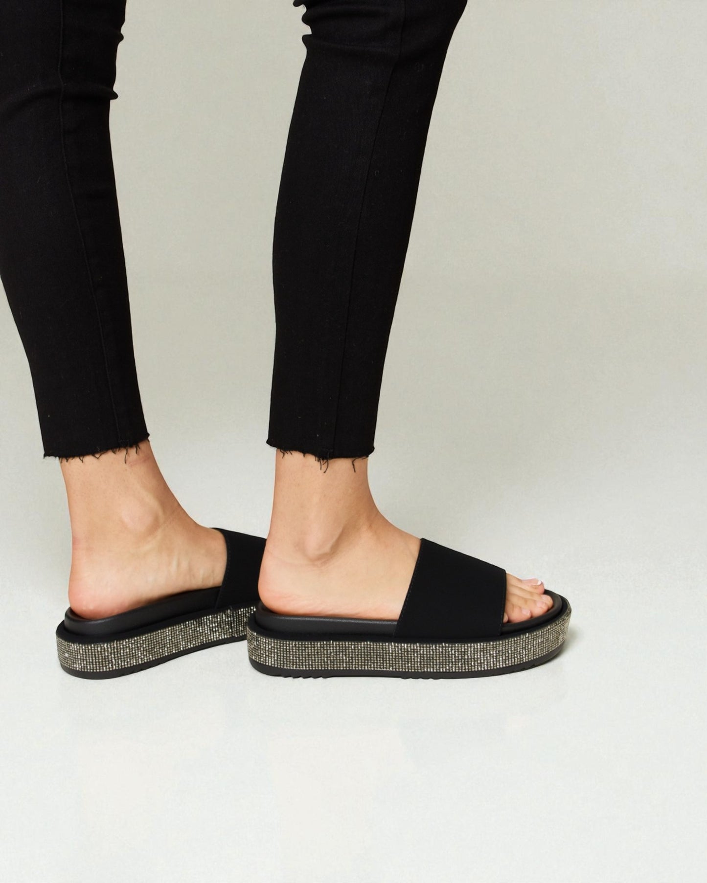 Black sandals worn with black pants on a plain background