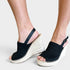A pair of women's black woven wedge sandals with braided jute espadrille-style wedge heels and ankle straps, shown worn on a model's feet against a light gray studio background.