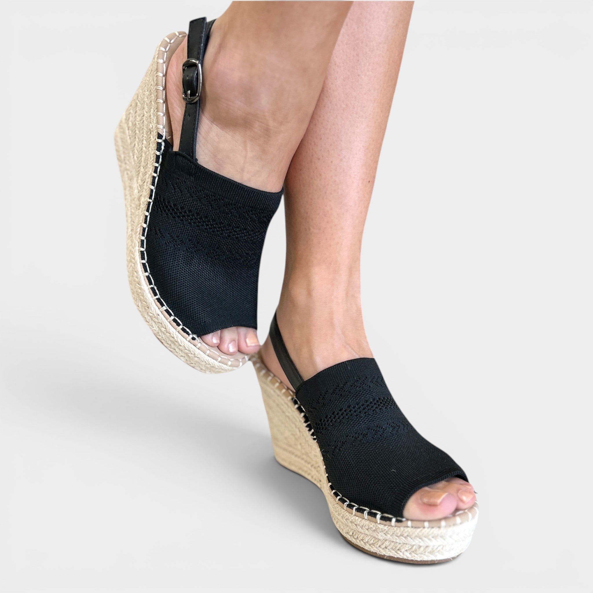 A pair of women's black knit wedge espadrilles with woven jute platform soles, shown on a model's feet against a light gray background.