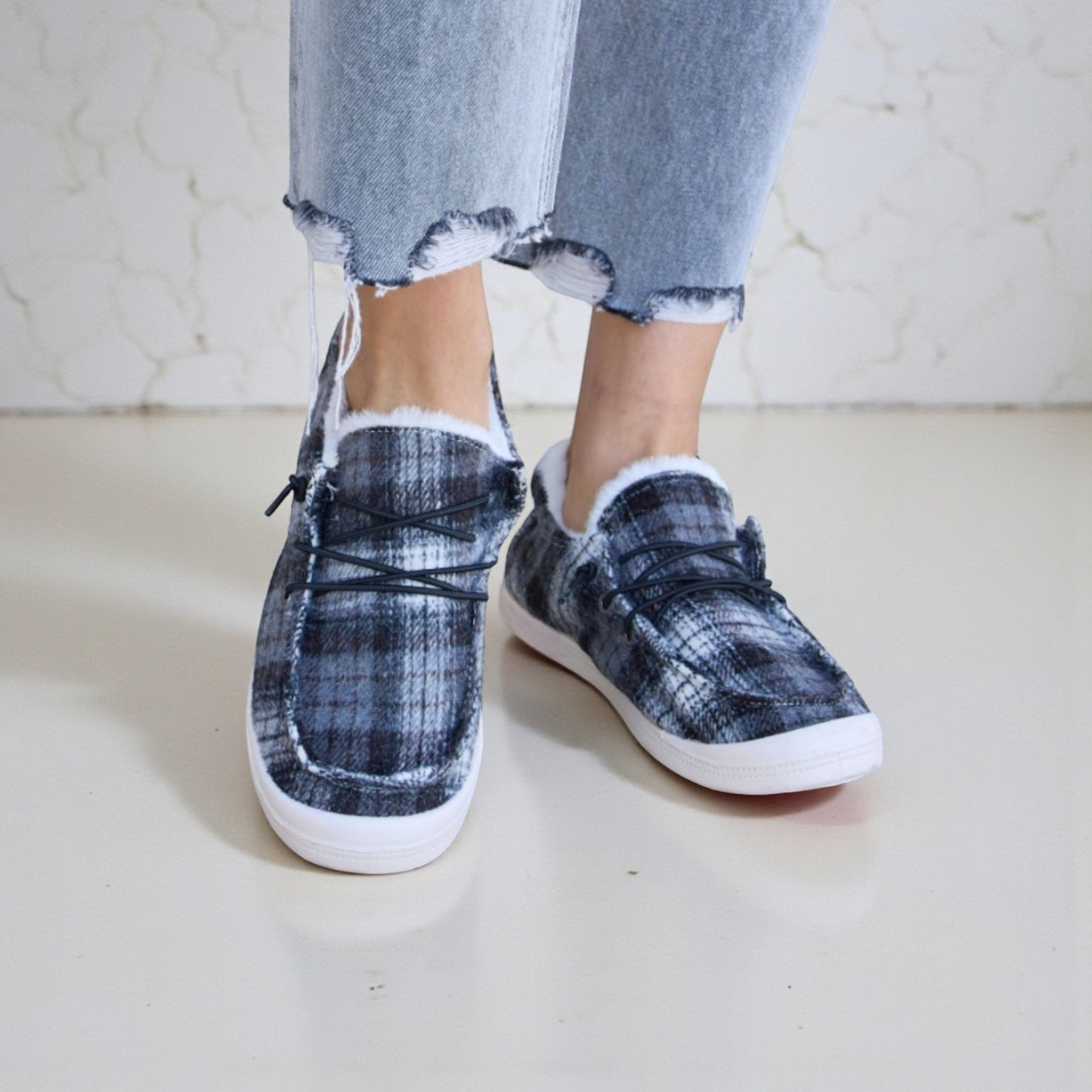 Plaid slip-on shoes worn with ripped jeans on a light background
