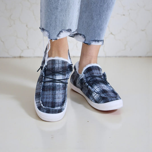 Plaid slip-on shoes worn with ripped jeans on a light background