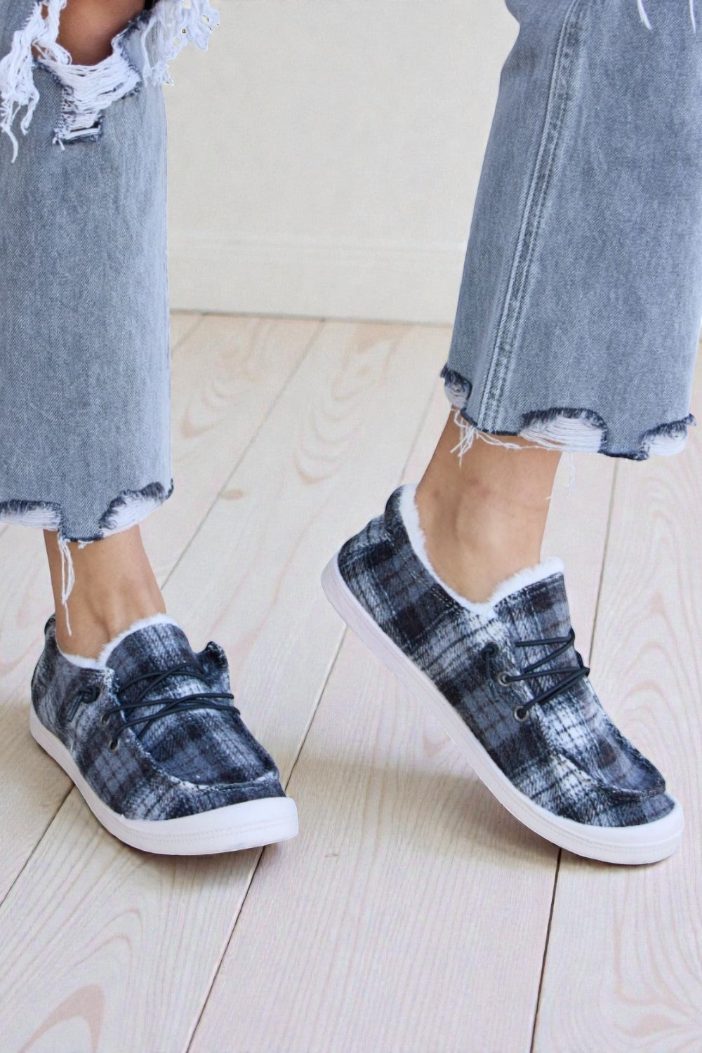 Plaid slip-on shoes worn with ripped jeans on a light wooden floor.
