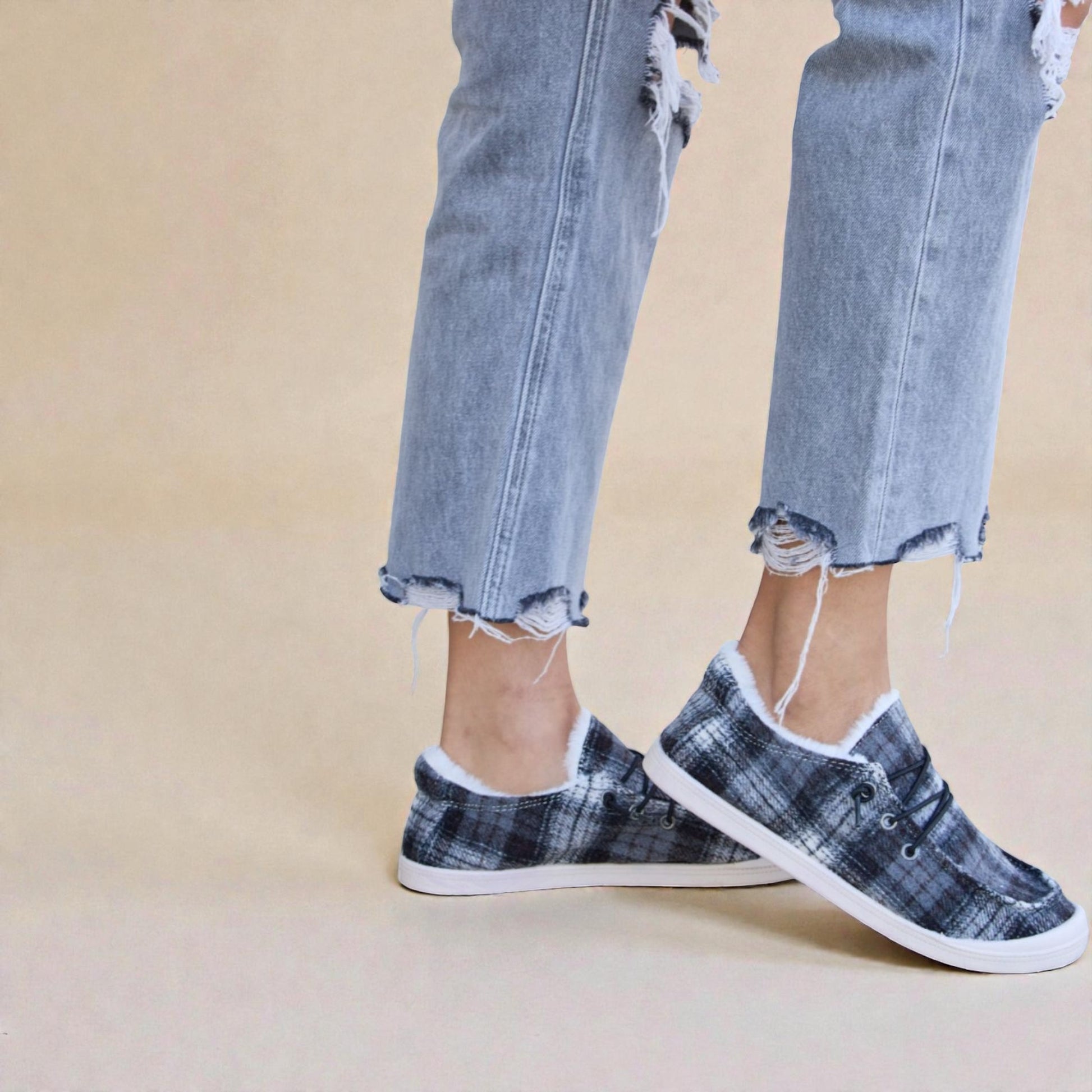 Person wearing plaid sneakers with ripped jeans on a beige background