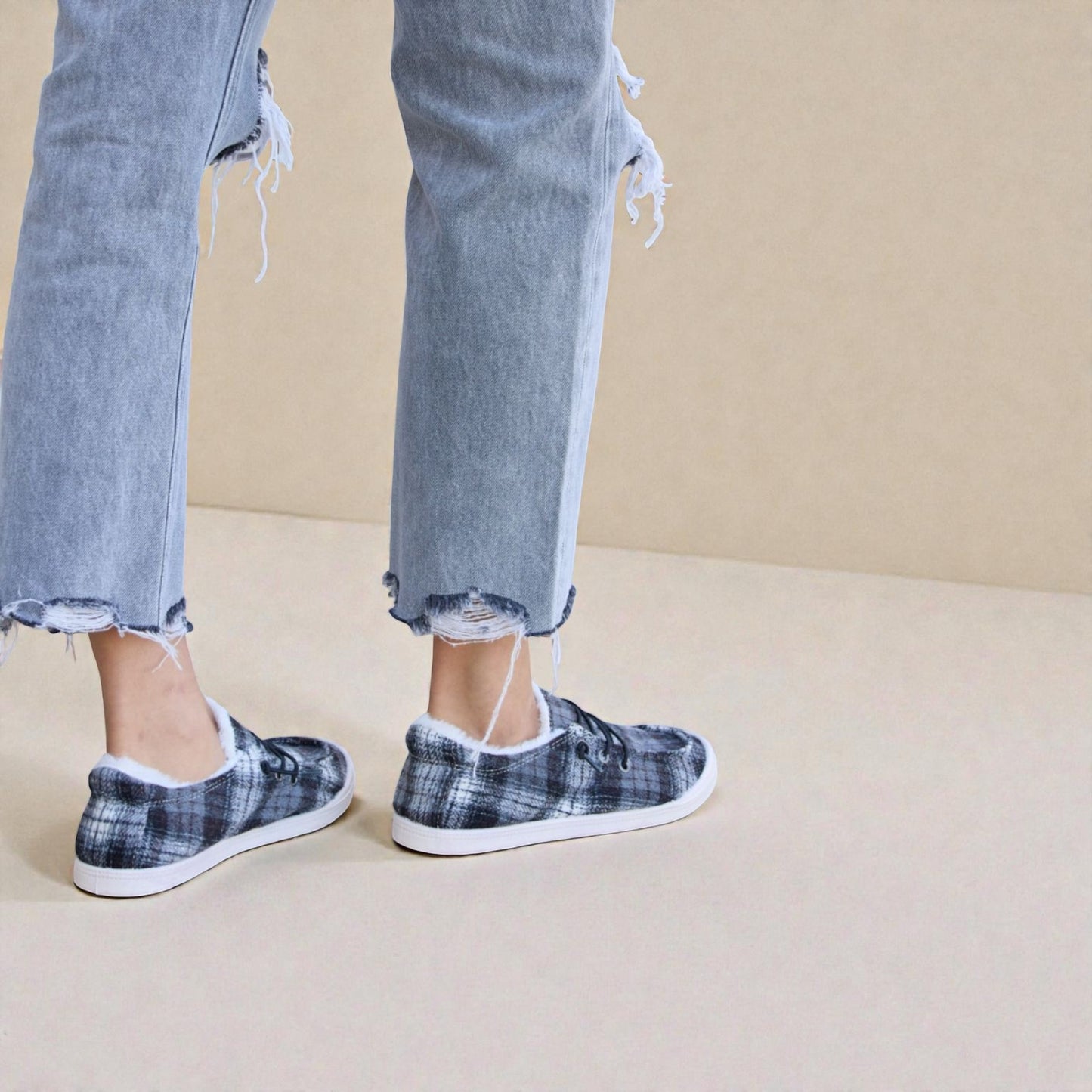 Person wearing plaid slip-on shoes with frayed jeans on a beige background