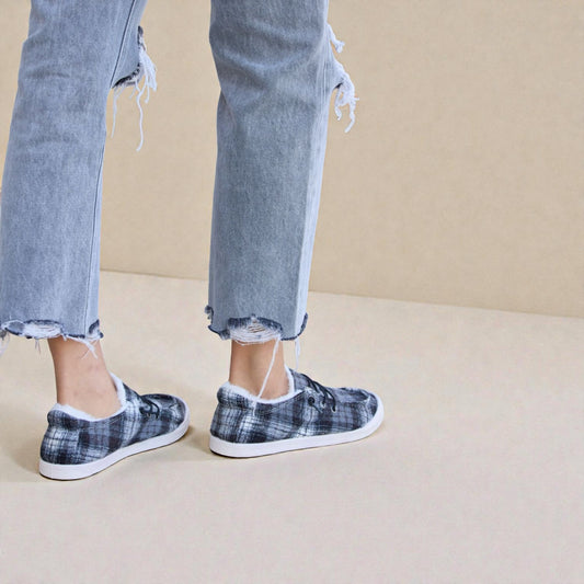 Person wearing plaid slip-on shoes with frayed jeans on a beige background