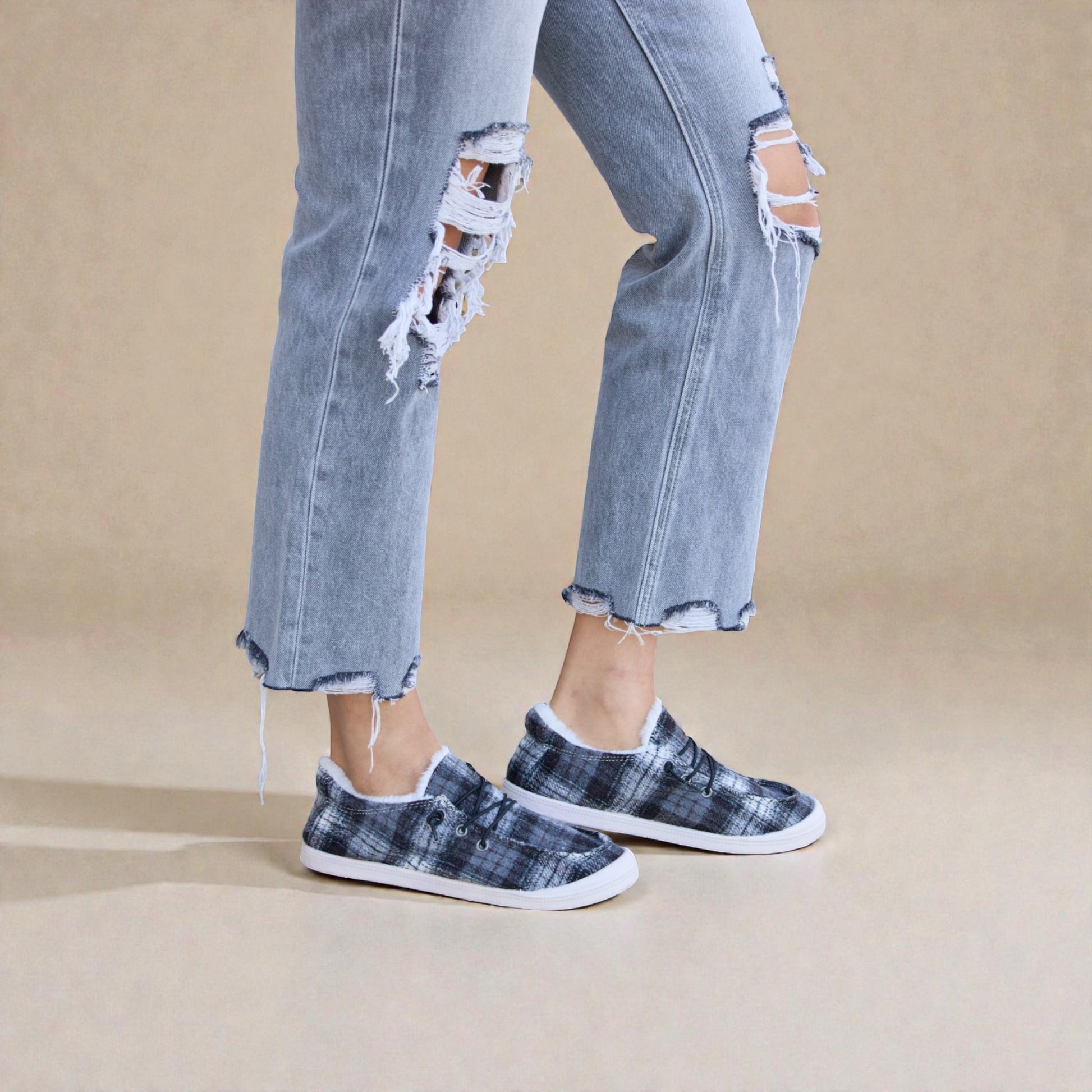 Person wearing ripped jeans and patterned slip-on shoes on a beige background