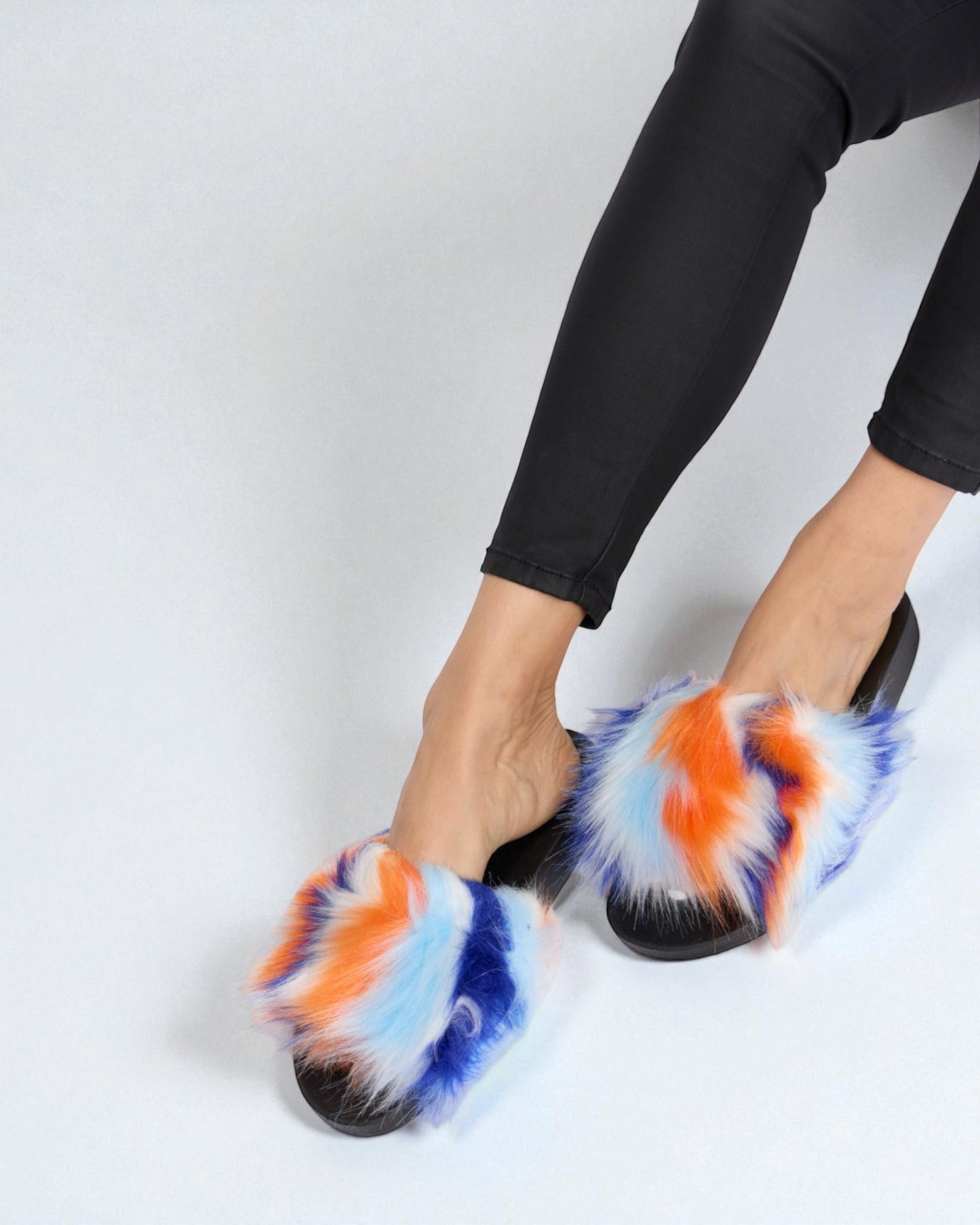 Multicolored fuzzy slippers worn with black pants on a light gray background