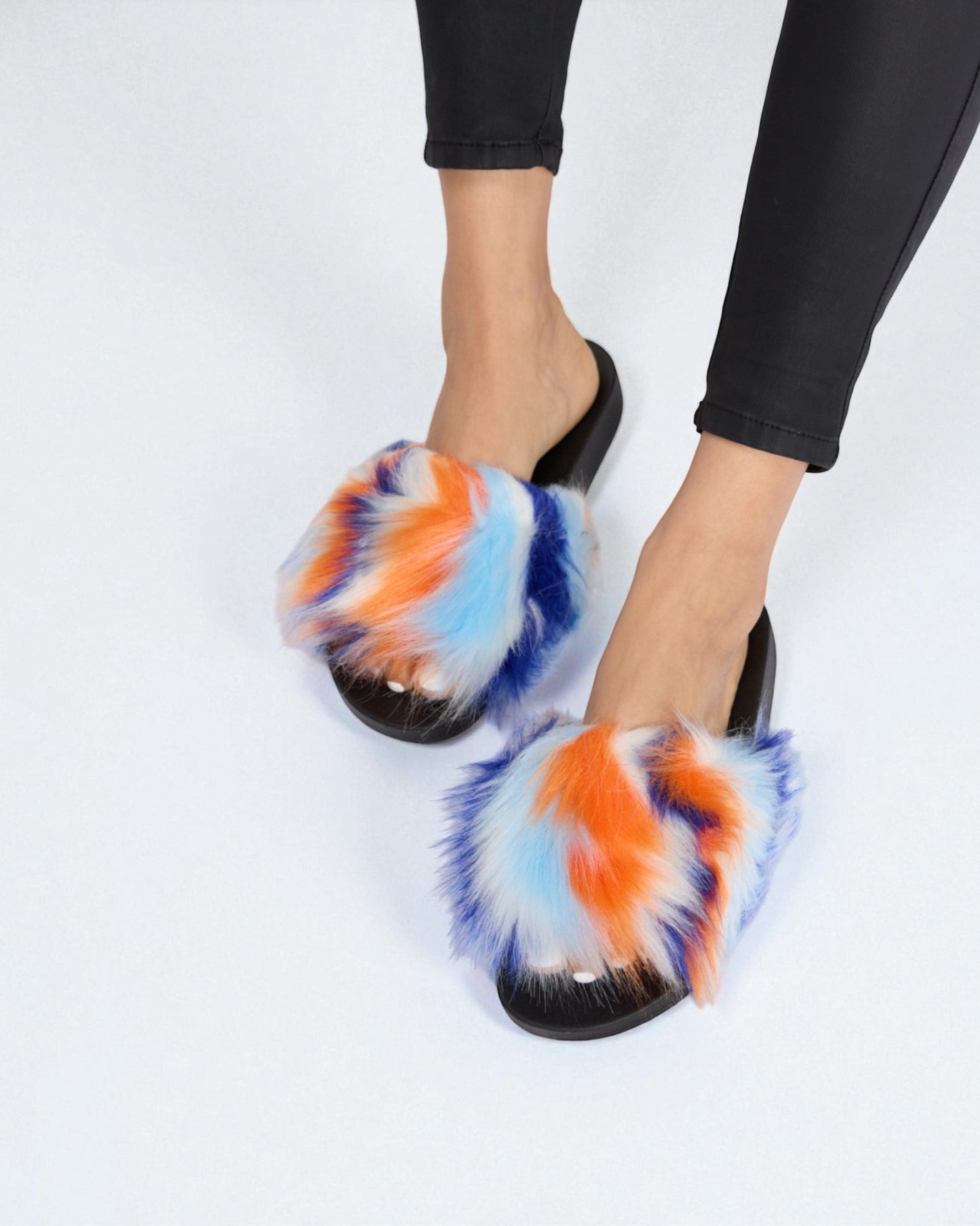Colorful tie-dye slippers worn with black pants on a white background