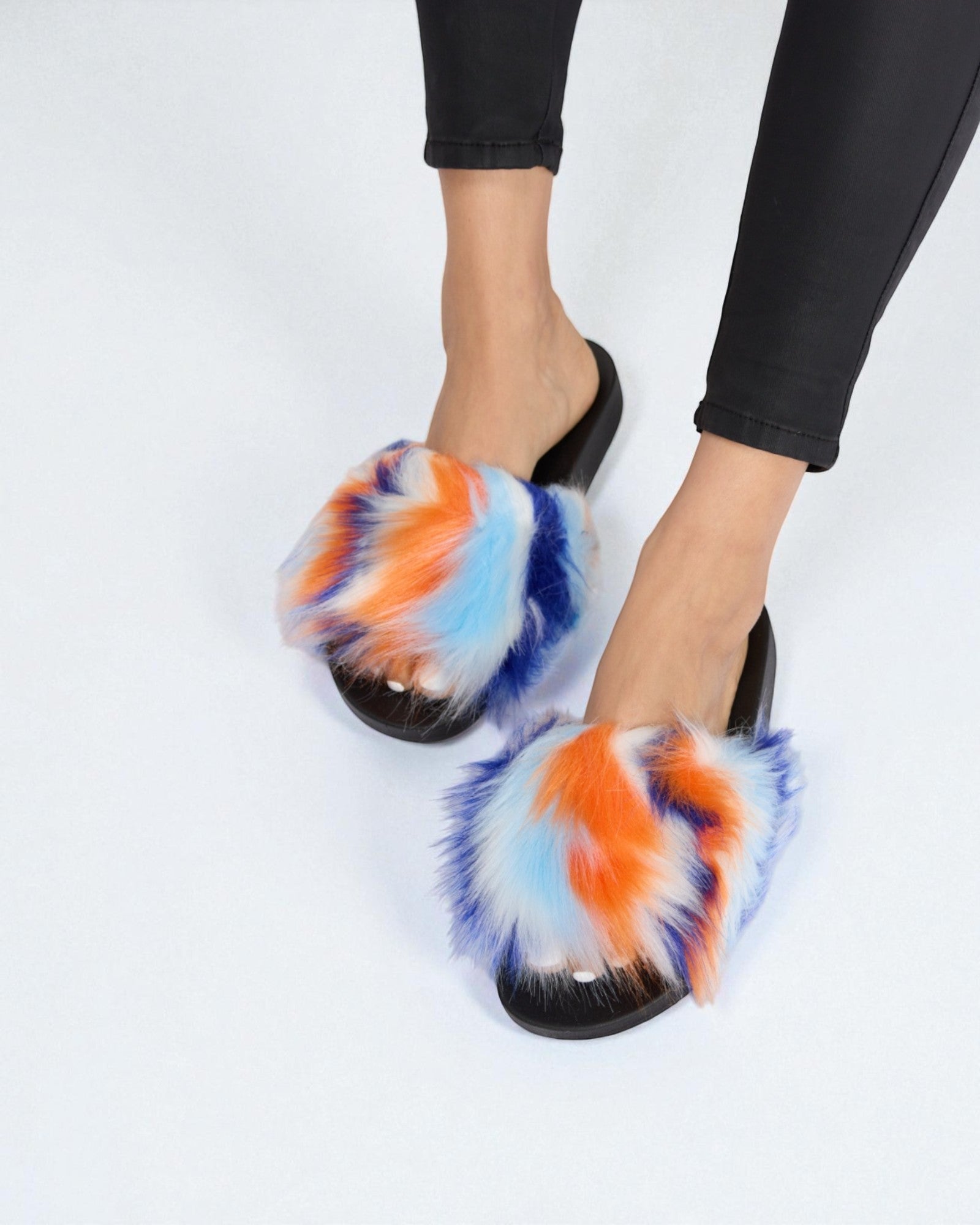 Colorful tie-dye slippers worn with black pants on a white background