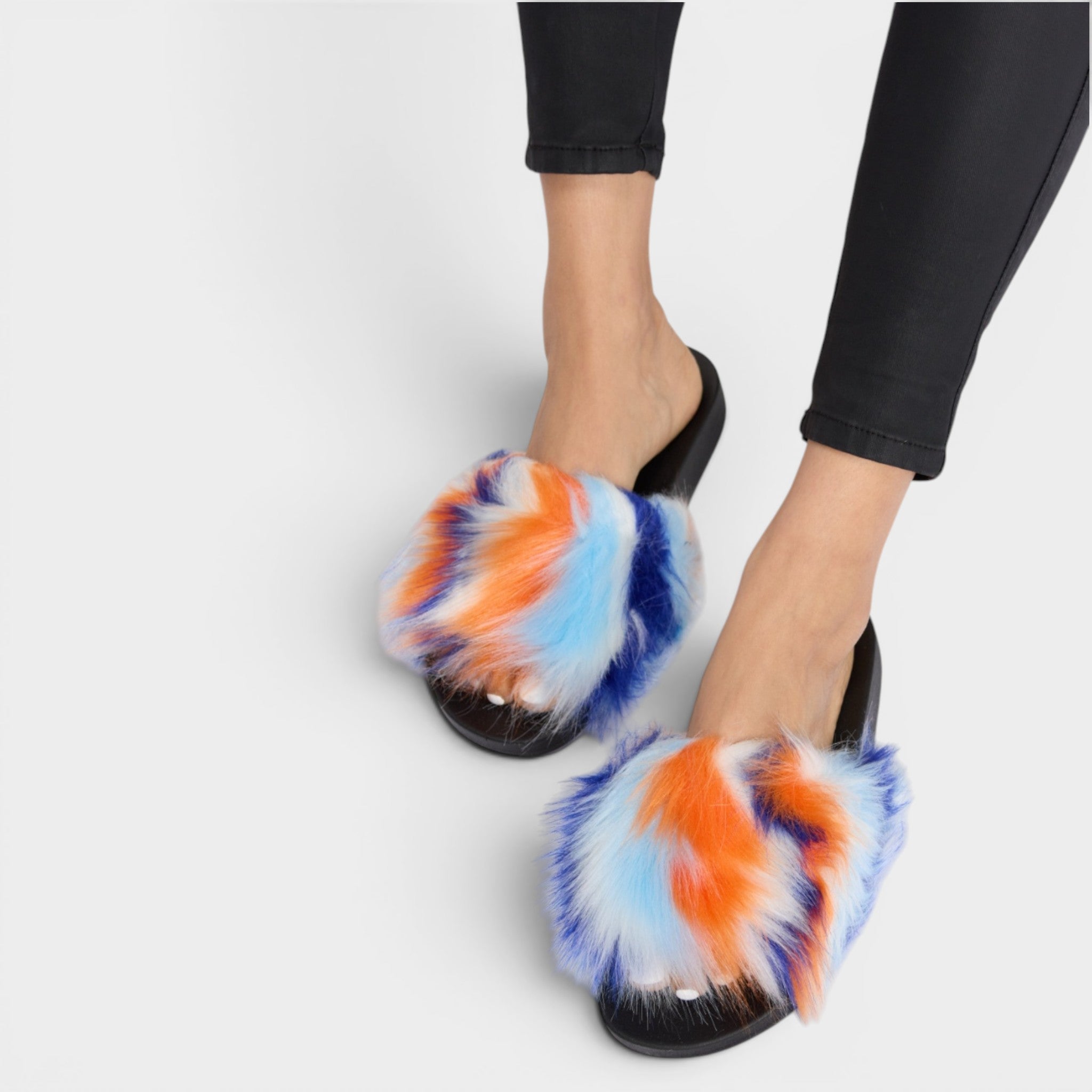 Colorful tie-dye slippers worn with black pants on a white background
